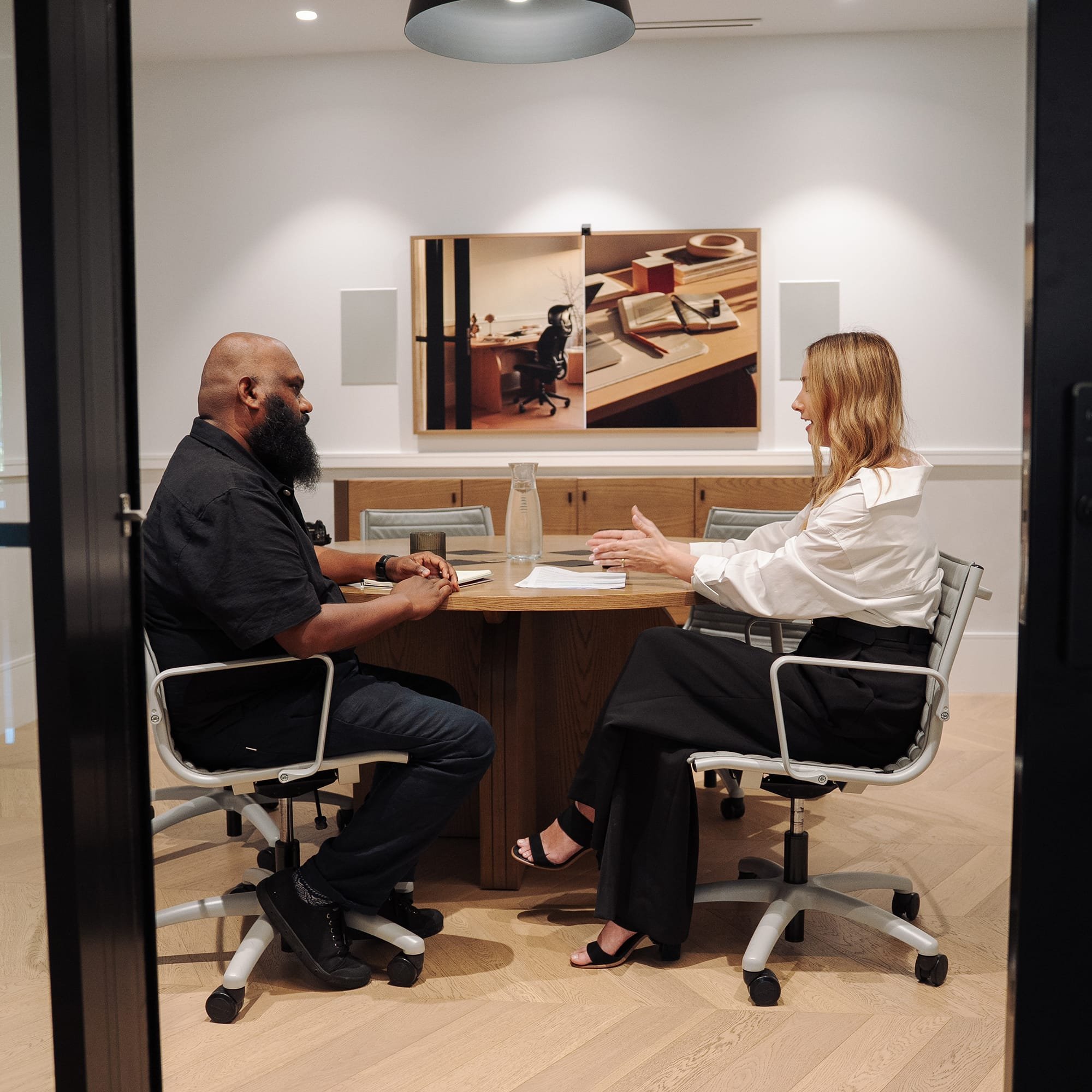Leadership coach facilitating a one on one workplace conversation at a conference table, focused on communication skills and professional development