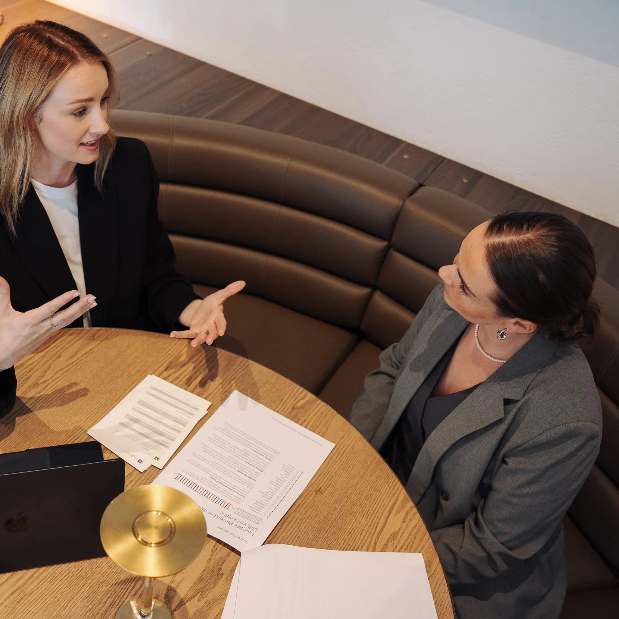 Facilitator guiding a workplace communication and leadership discussion at a round table with documents and a laptop