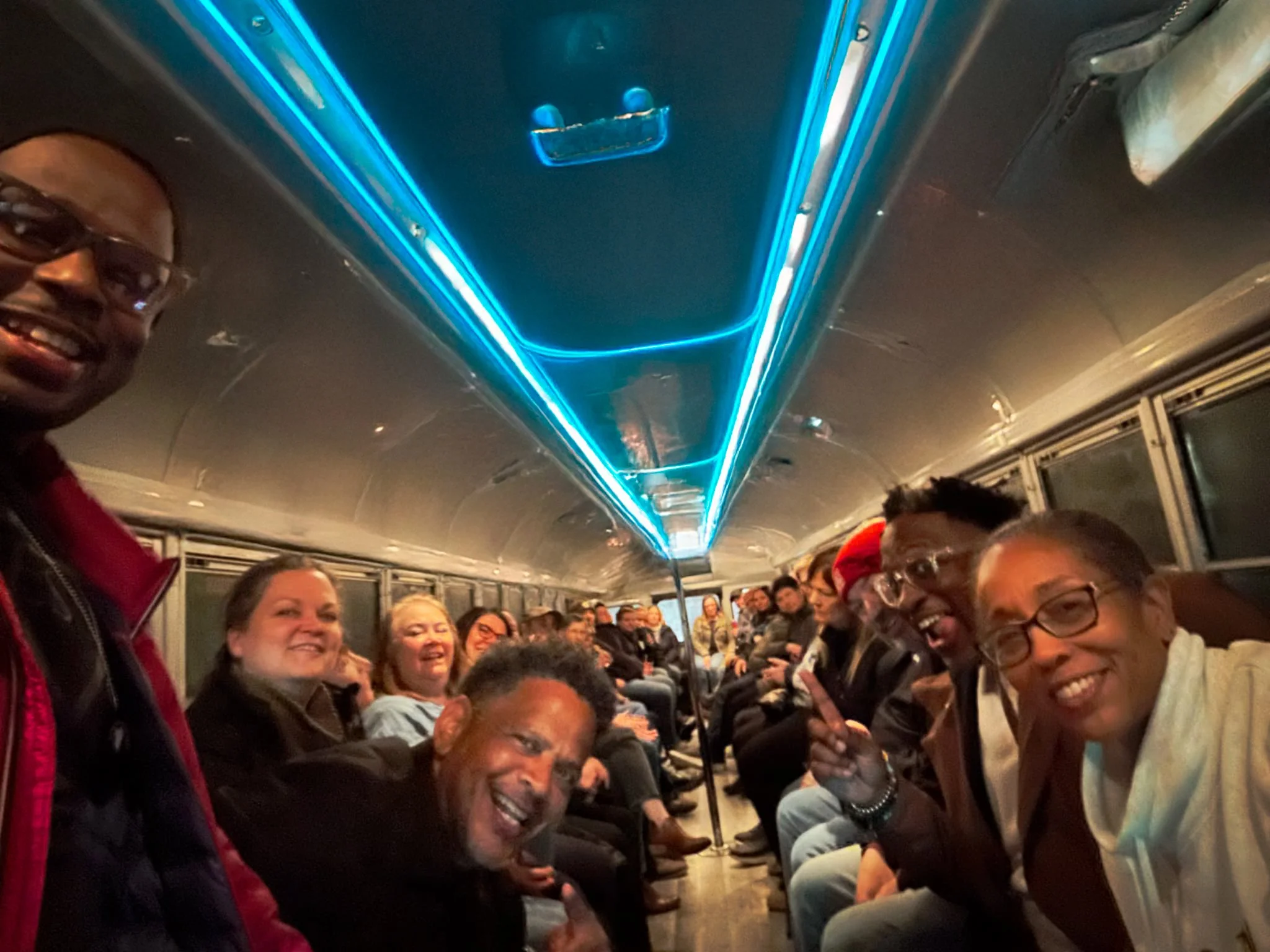 Group of people smiling and enjoying a party on a bus with neon blue lighting.