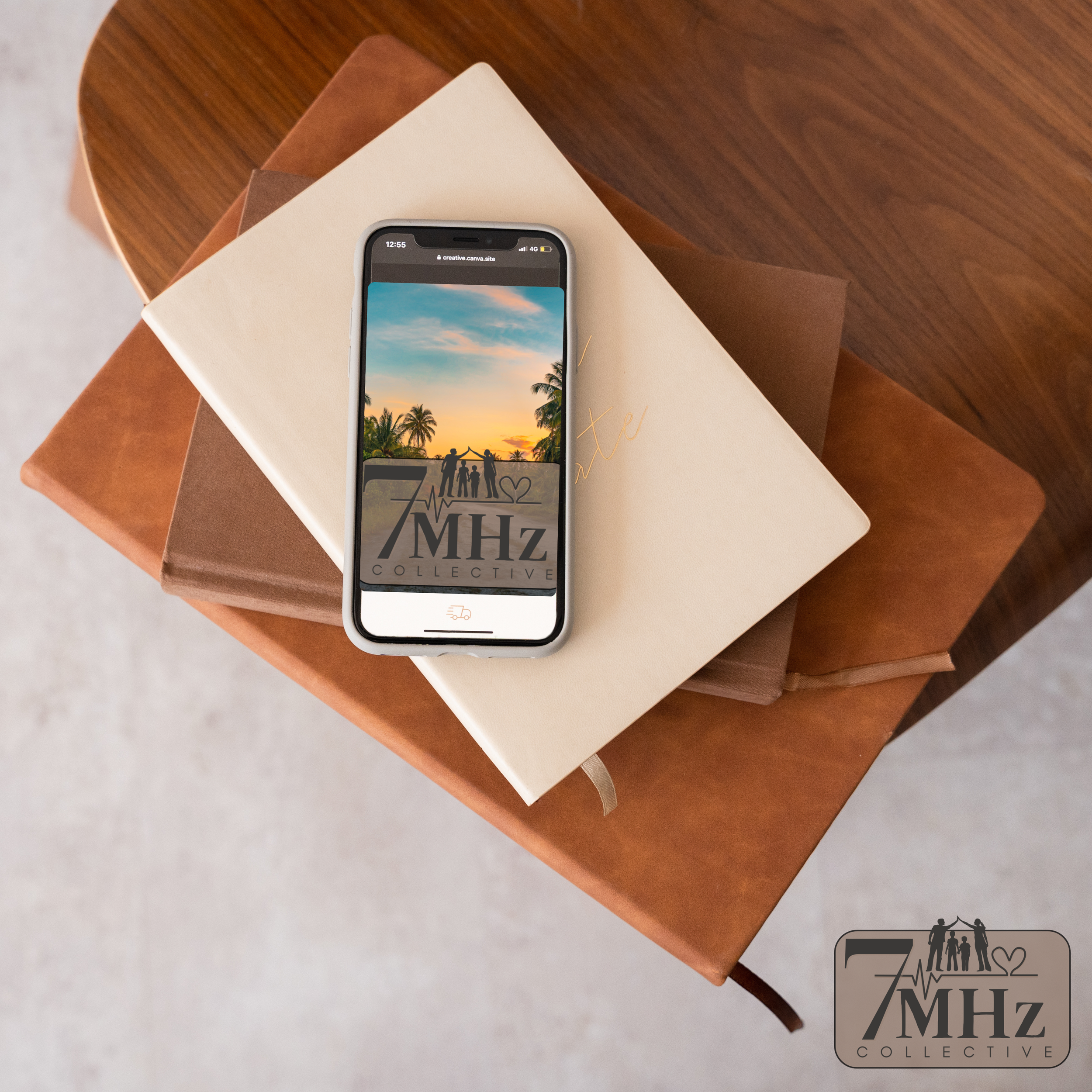 An iPhone displaying a sunset scene with palm trees and silhouettes of people, resting on a stack of notebooks on a wooden table, with a logo of '7MHz Collective' on the screen and in the bottom right corner of the image.