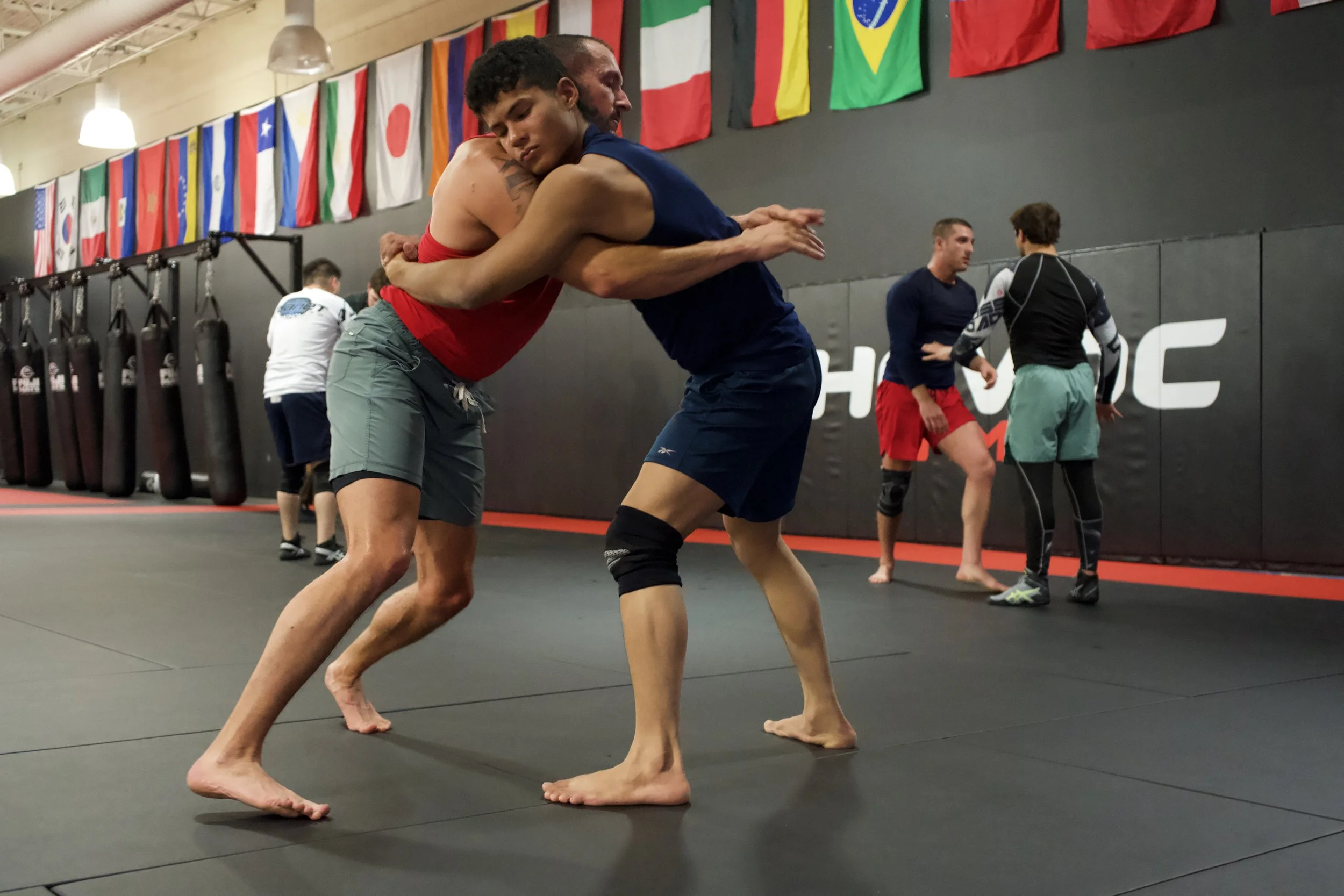 Man with long hair and tattoos smiling and pointing upward with both hands in a gym.