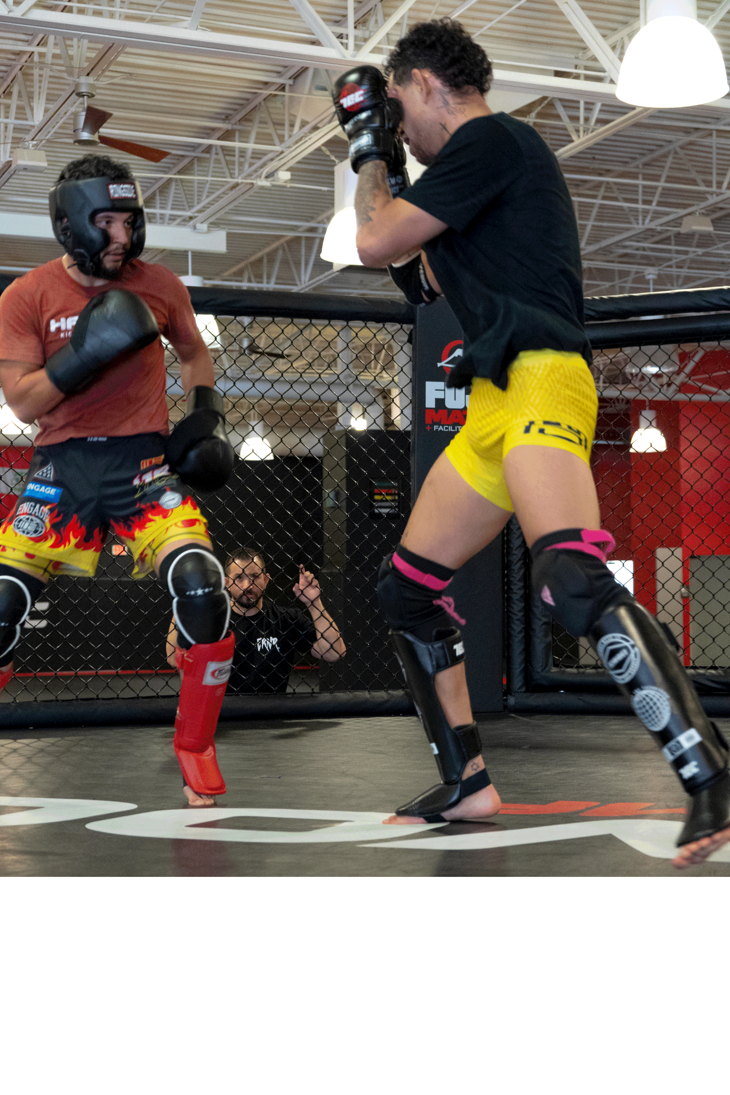 Two women training in a mixed martial arts cage, practicing striking techniques under the supervision of a coach.