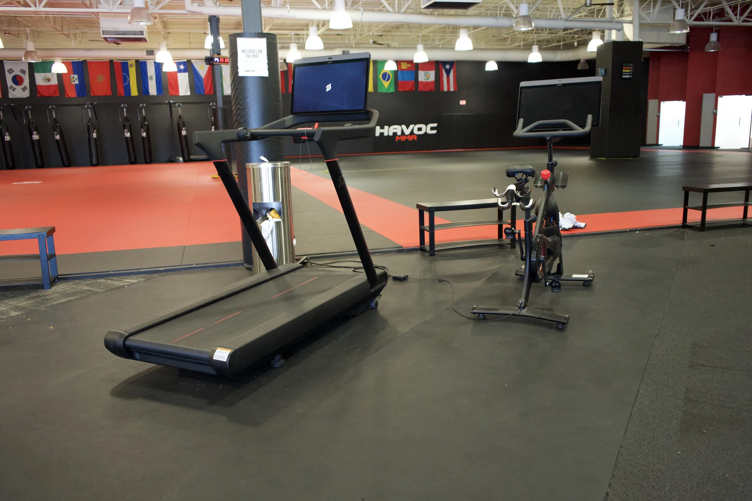 Empty gym with treadmill, exercise bike, benches, and flags hanging from ceiling at a martial arts gym.