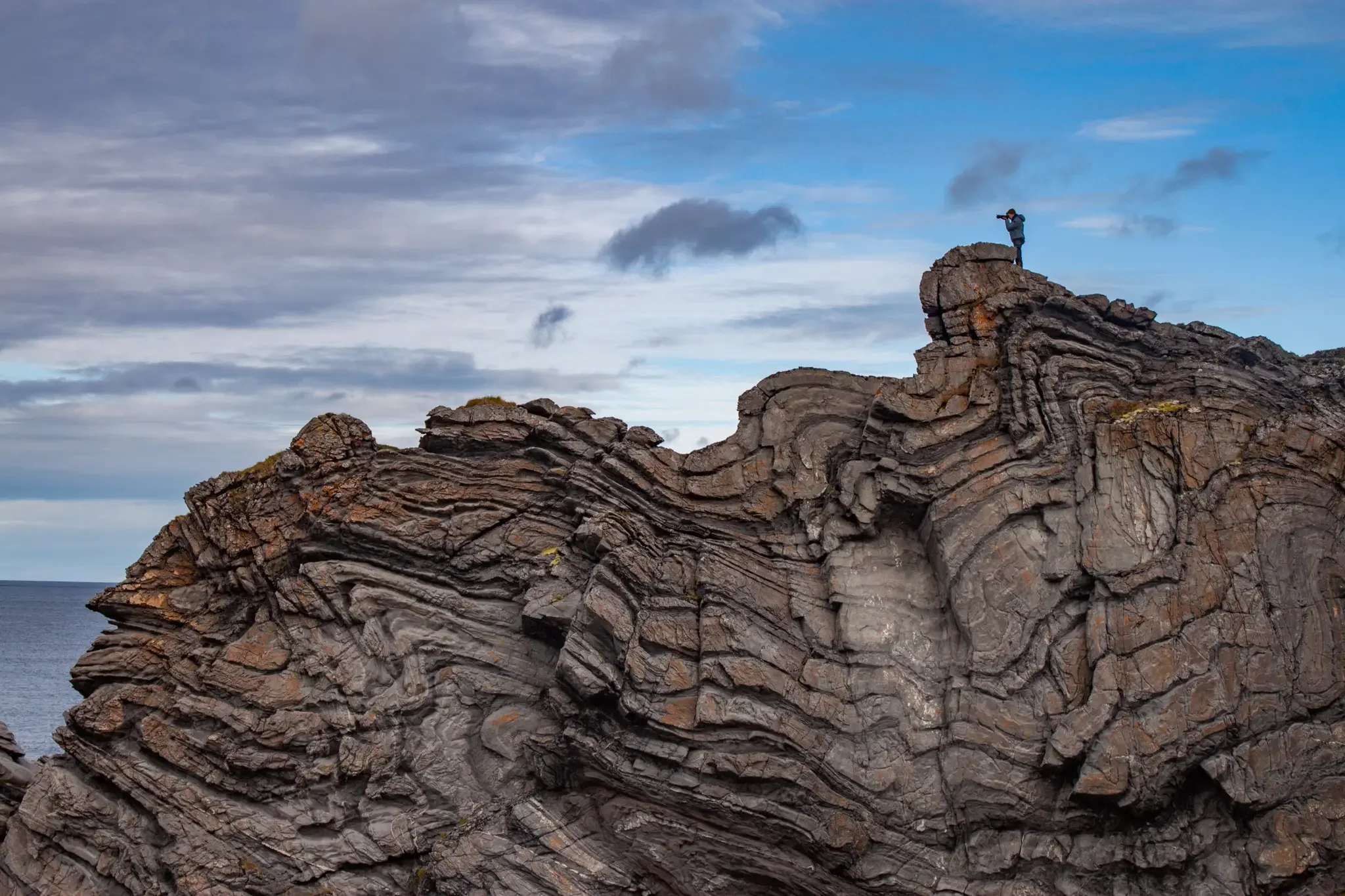 solo travel photographer on top of a huge rock formation aiming camera into the distance