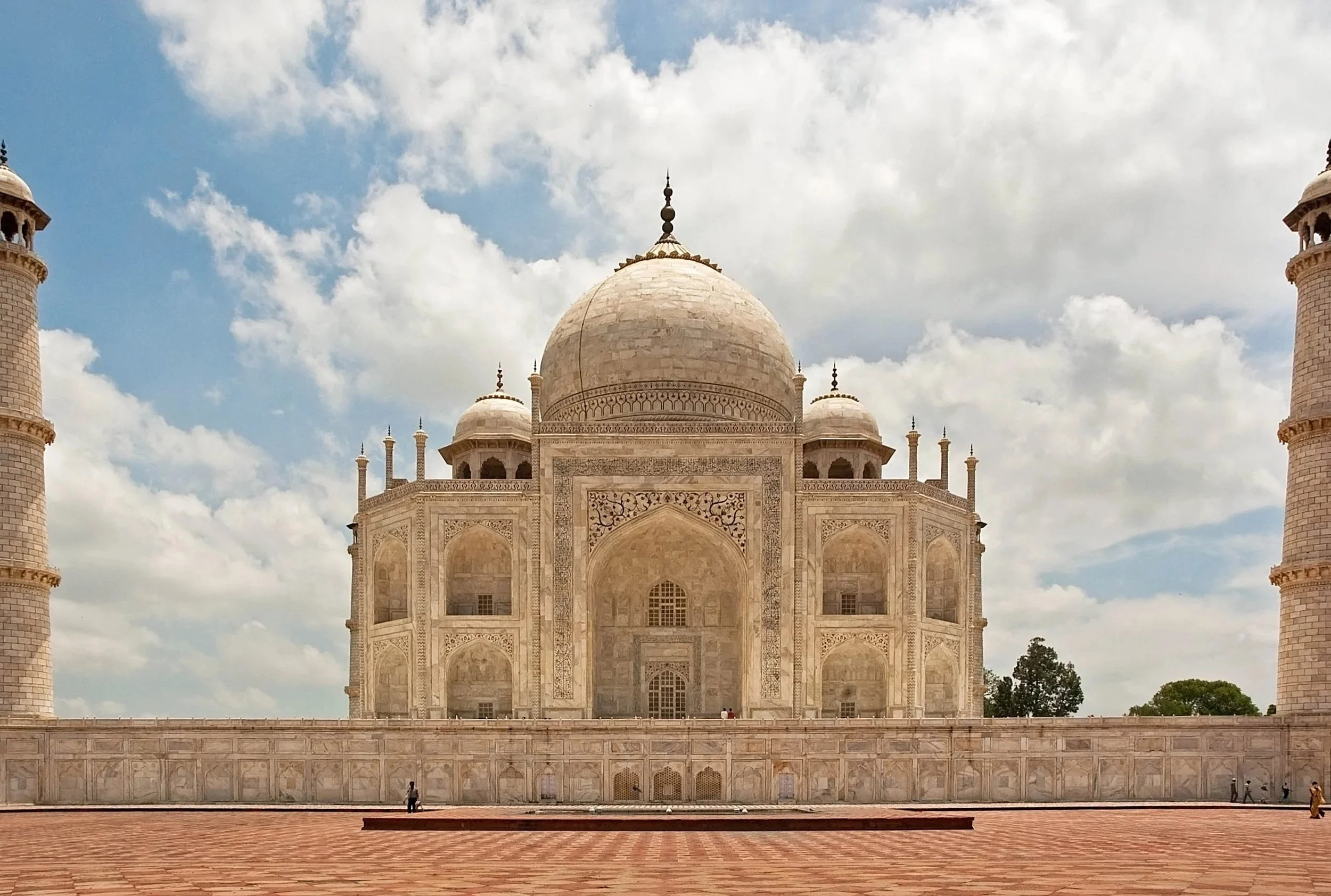 The Taj Mahal, a white marble mausoleum with a large central dome and four minarets, set against a partly cloudy sky.