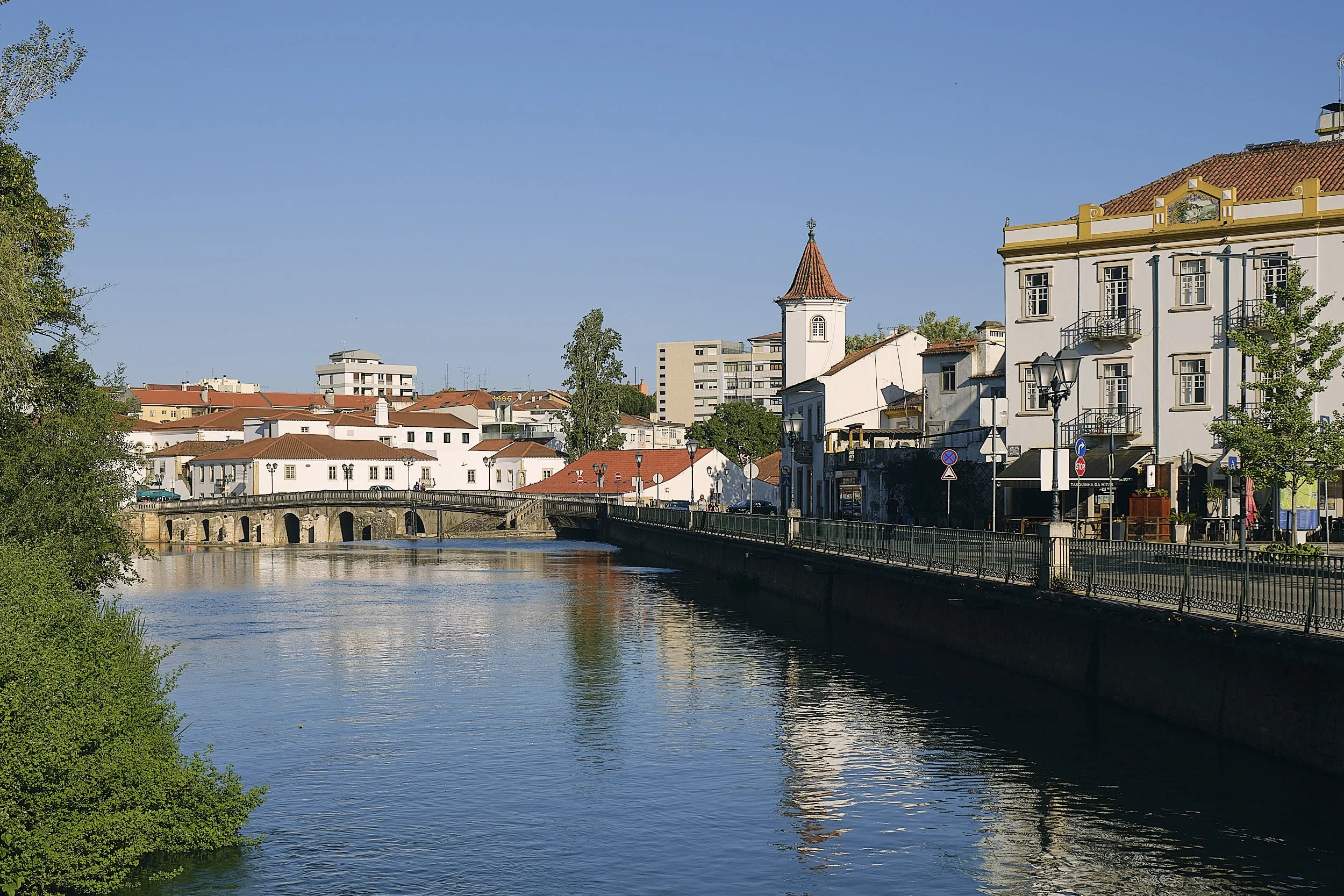 A scenic view of a river with historic buildings and a bridge, under a clear blue sky.