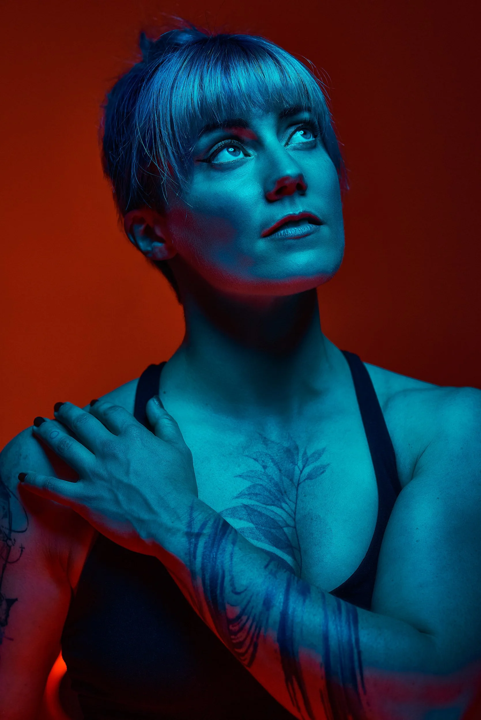 close up colourful editorial portrait of athletic strong acrobat, vivid Teal colour lighting subject with a deep Amber glow of light from underneath and behind on the background. Tatoos, muscle and expression. 