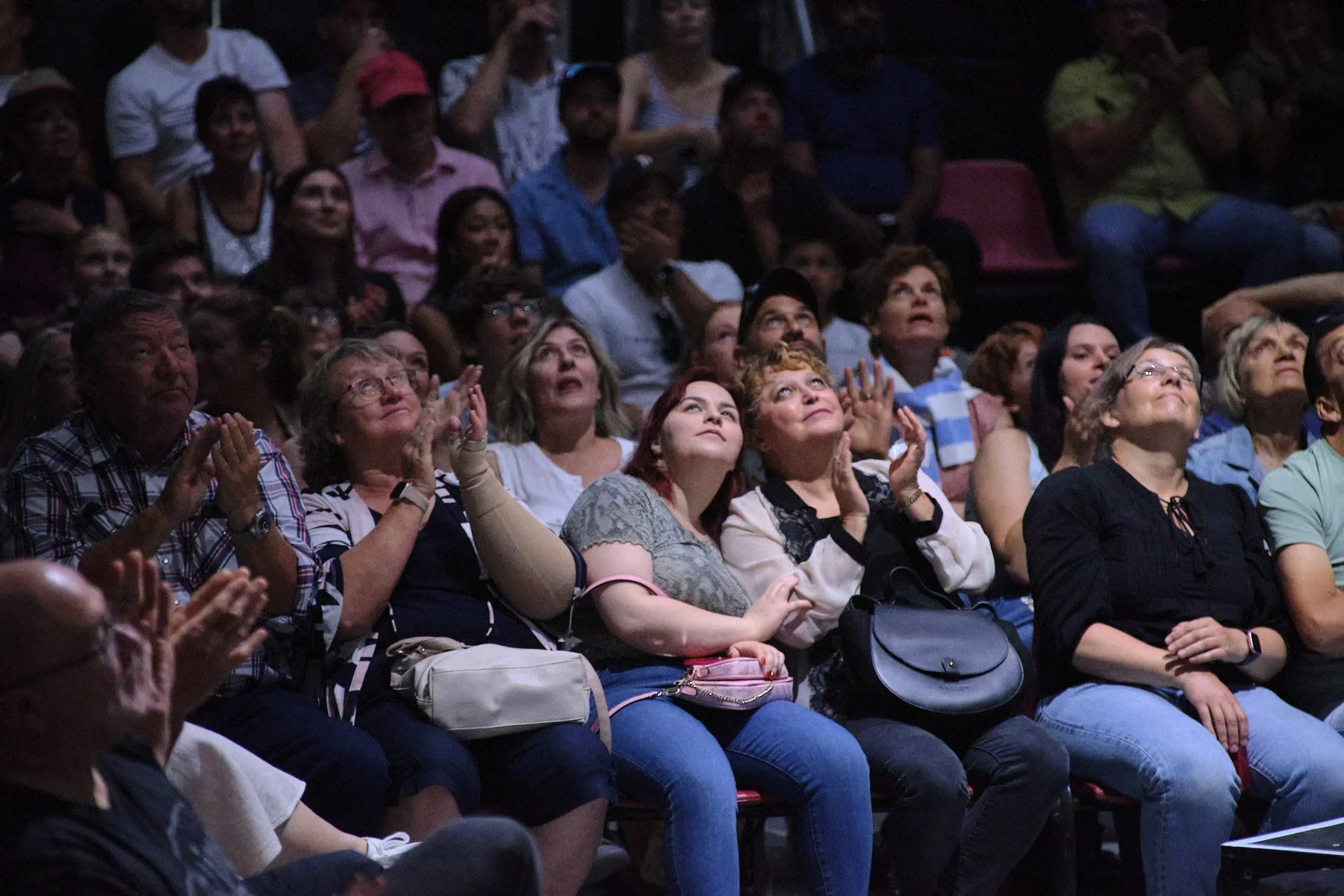 Audience watching a performance on stage, showing various reactions of interest and enjoyment.