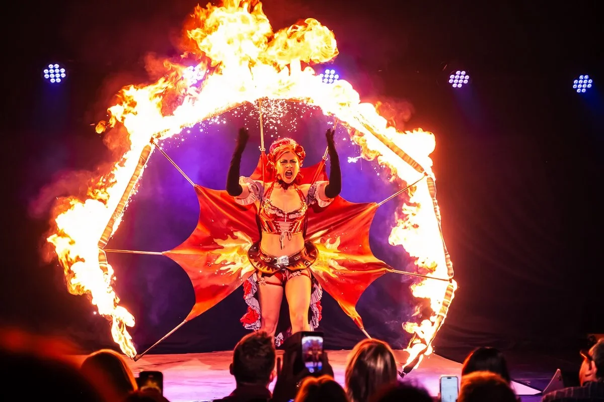 A fire performer on stage with a flaming prop, dressed in a colorful costume, entertaining an audience.