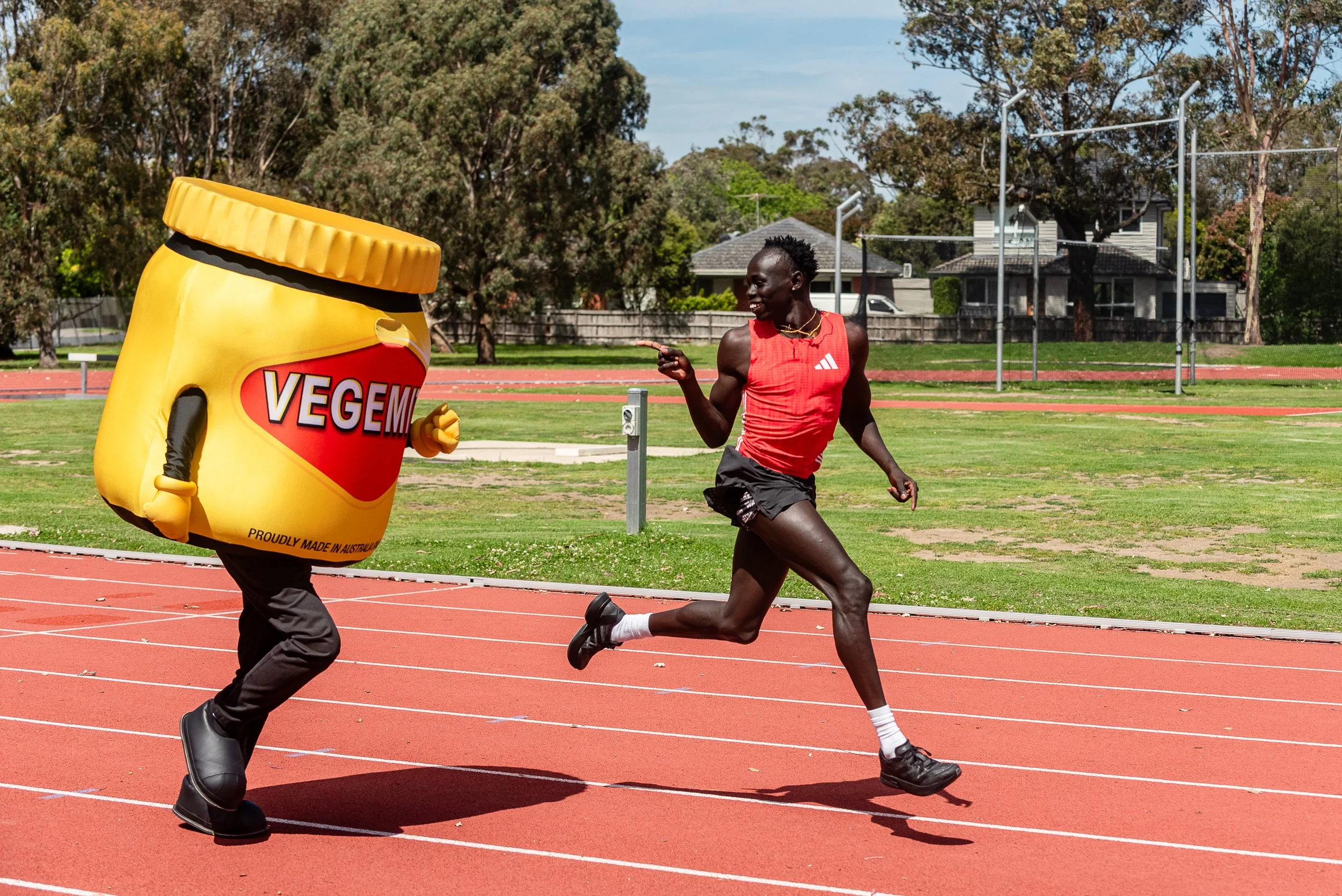 A person in a bee costume running on a track next to a woman in athletic clothing, outdoors during the day.