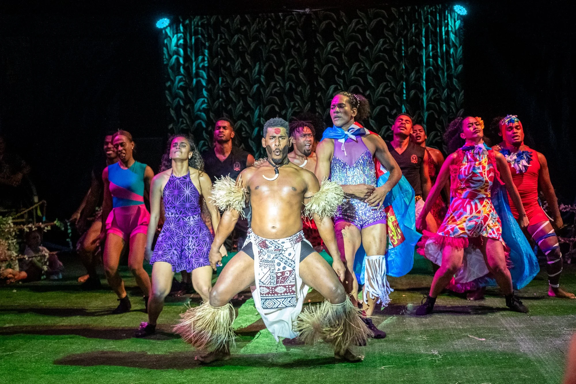 Group of performers in colorful costumes on stage during a cultural dance performance at night.