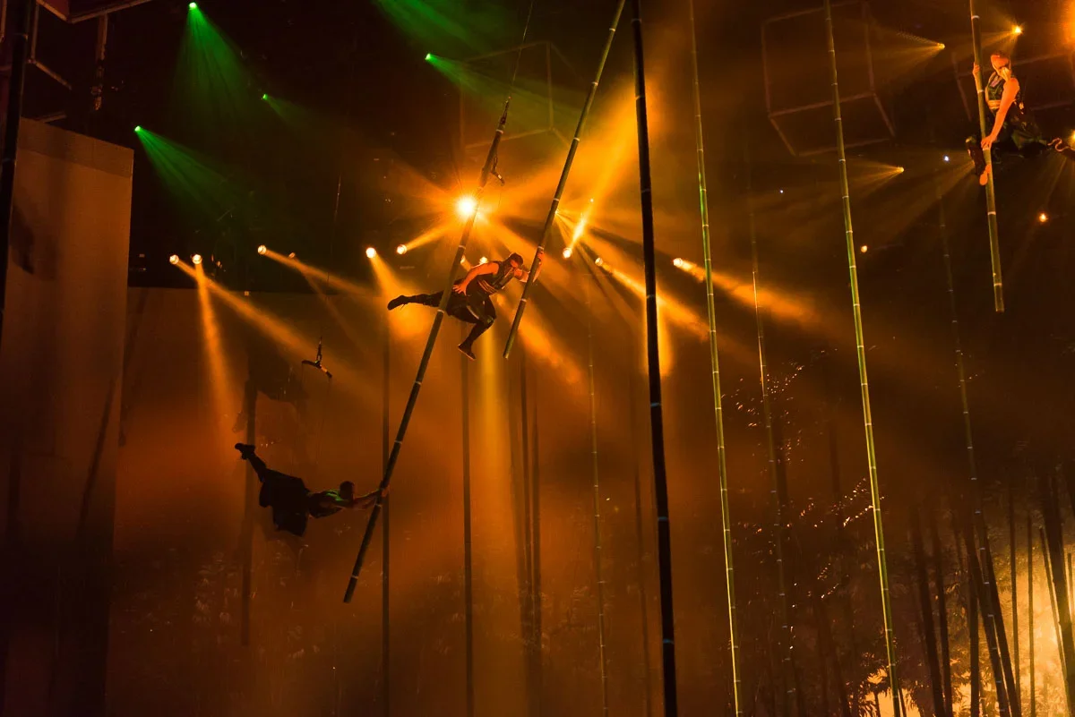 Circus performers practicing aerial silk routines with ropes and poles under warm stage lighting.
