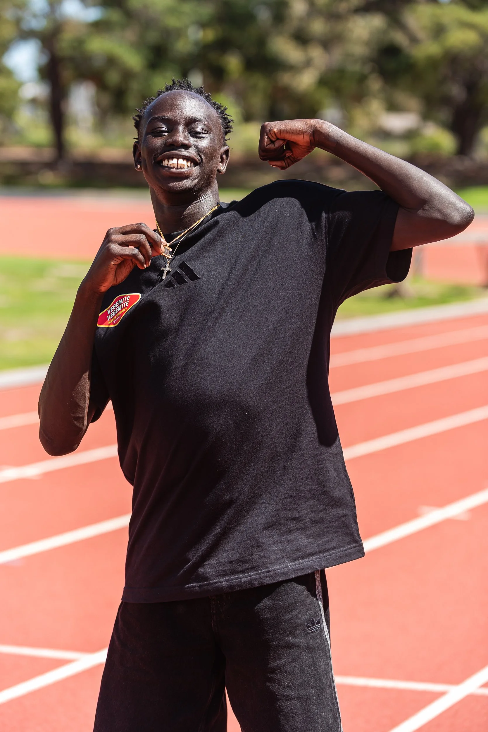 A person smiling and flexing their arm while standing on a running track.