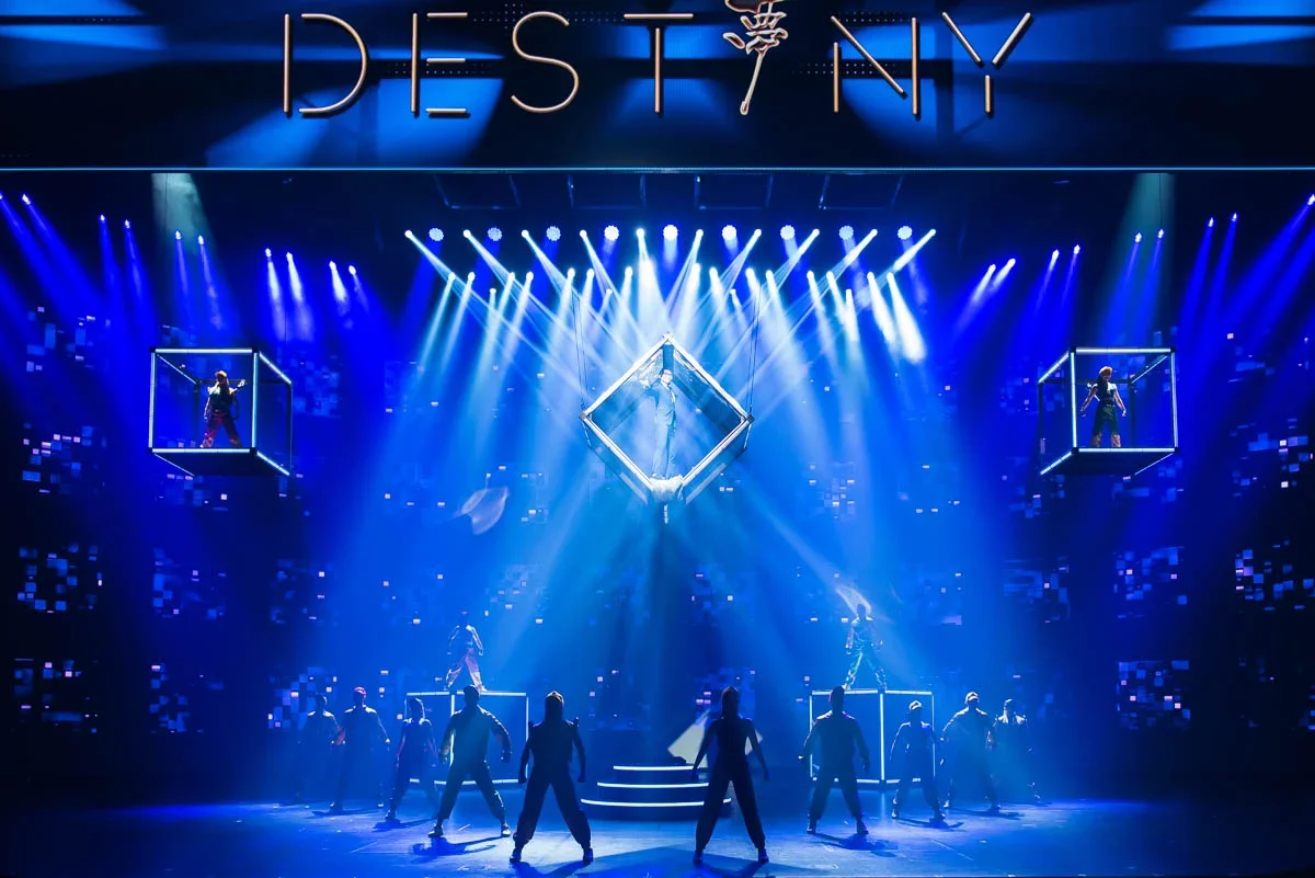 Stage with performers in a light show, illuminated by blue lights; large sign reads 'DESTINY'.
