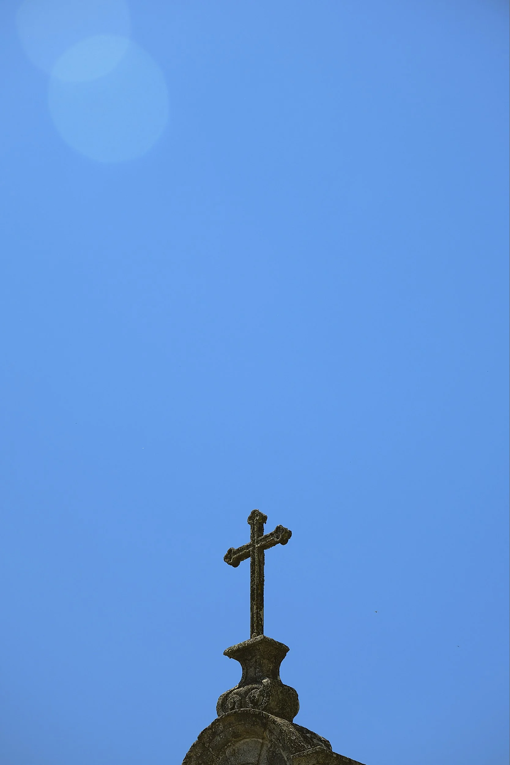 A stone cross mounted on the top of a church steeple against a clear blue sky.