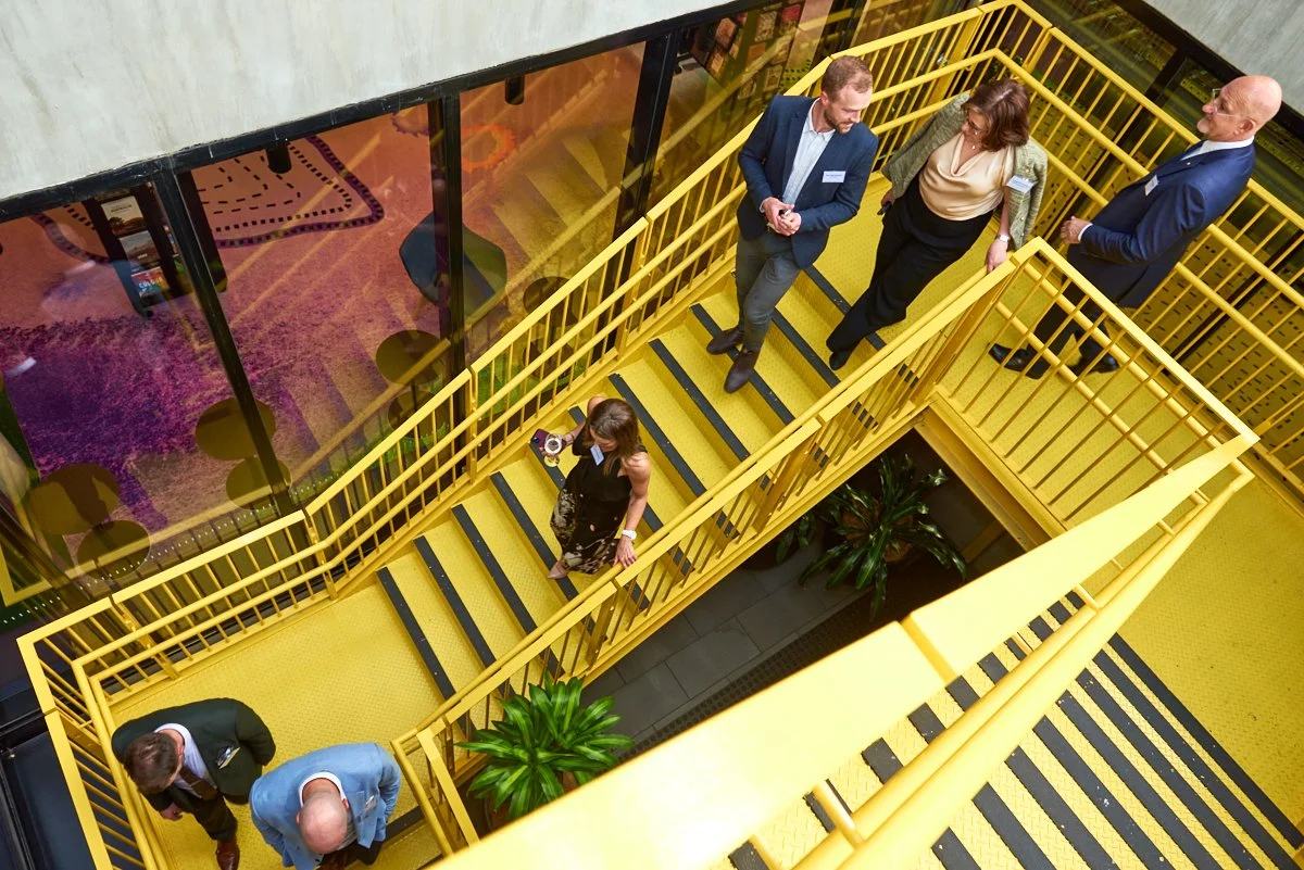People in business attire walking and talking on a yellow staircase in an office building.
