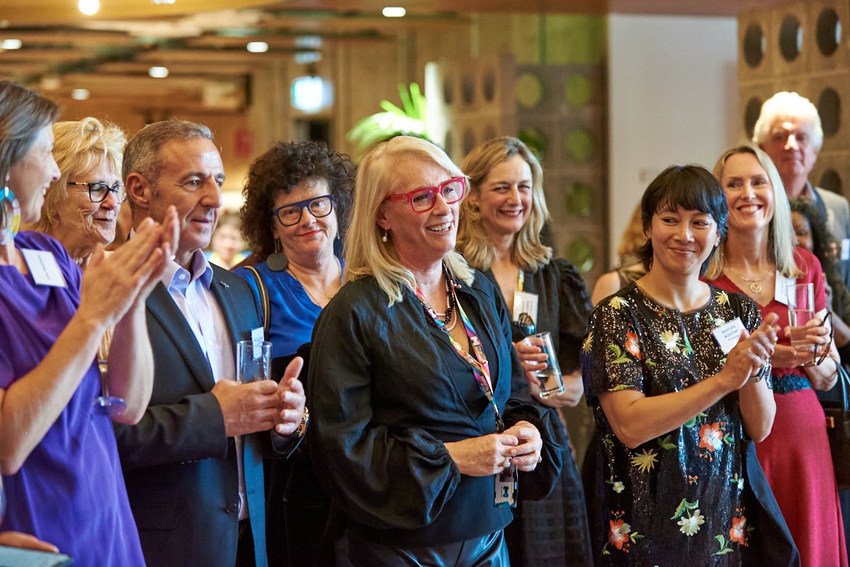 Group of professionally dressed adults at a social or corporate event, smiling and holding glasses for a toast or drink.