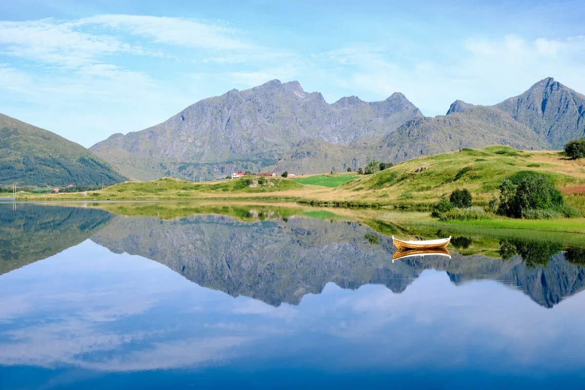 A calm lake reflecting green hills and mountains in the background with a small boat floating on the water.
