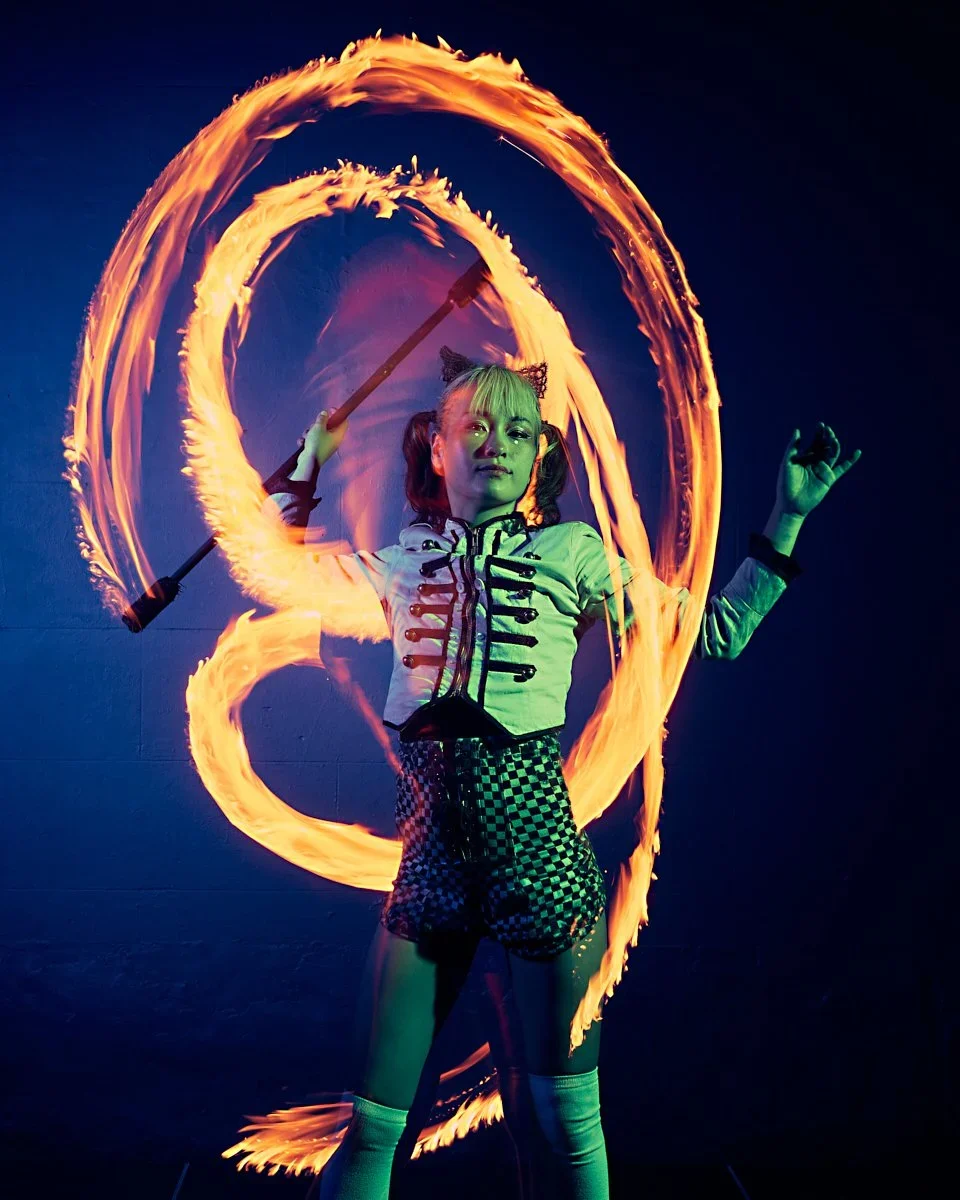 A girl performing a fire spinning act, creating fiery rings with a fire poi against a dark background.