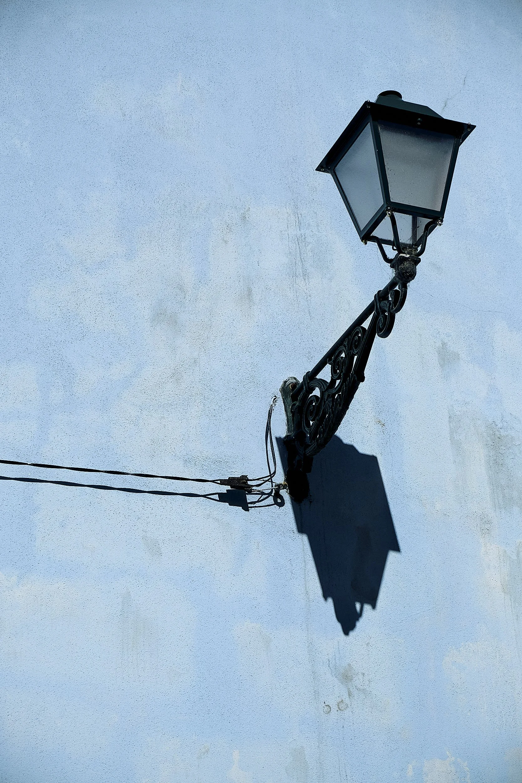 A black vintage-style street lantern attached to a weathered light blue wall, casting a shadow.