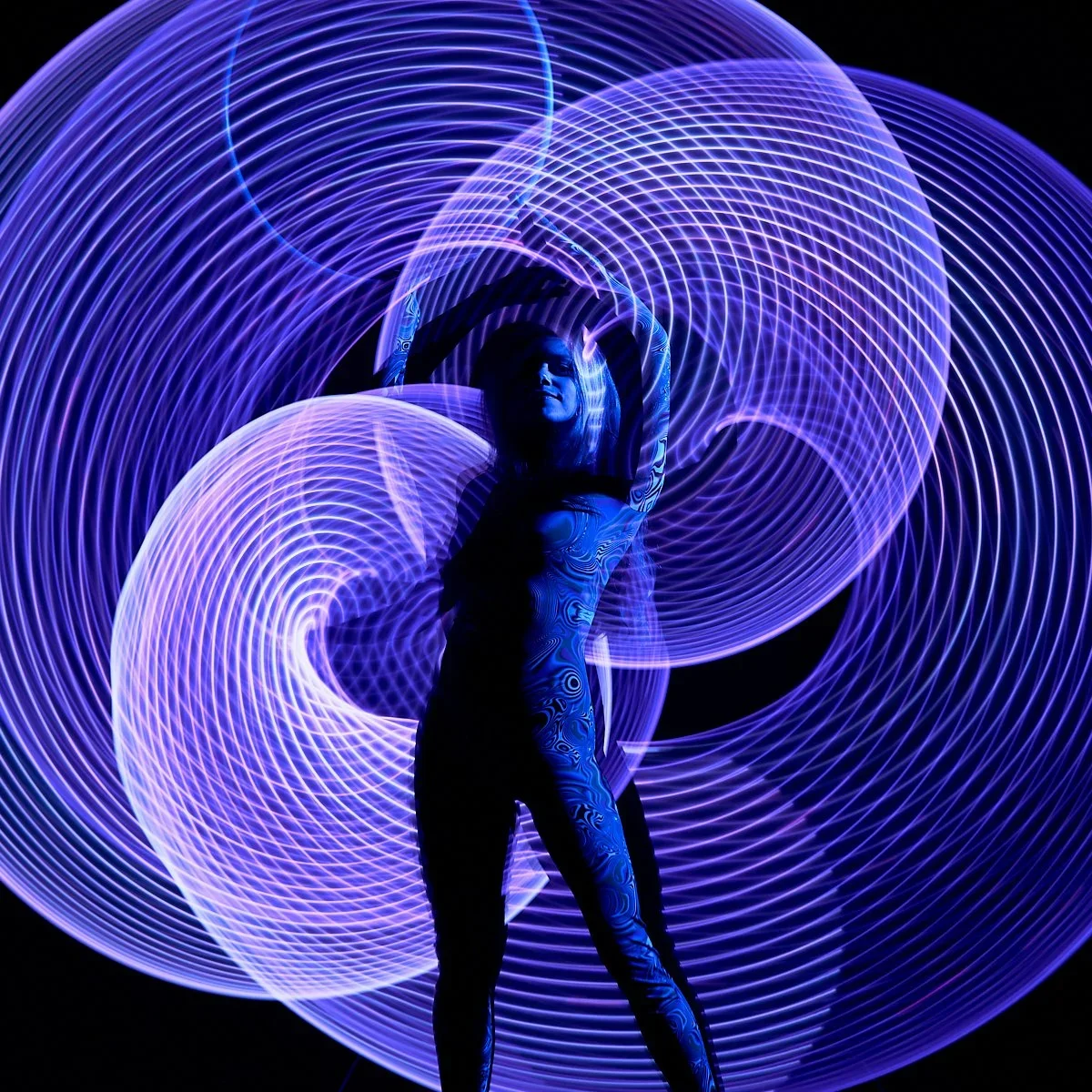 A woman posing against a backdrop of purple and blue light streaks creating swirling patterns.
