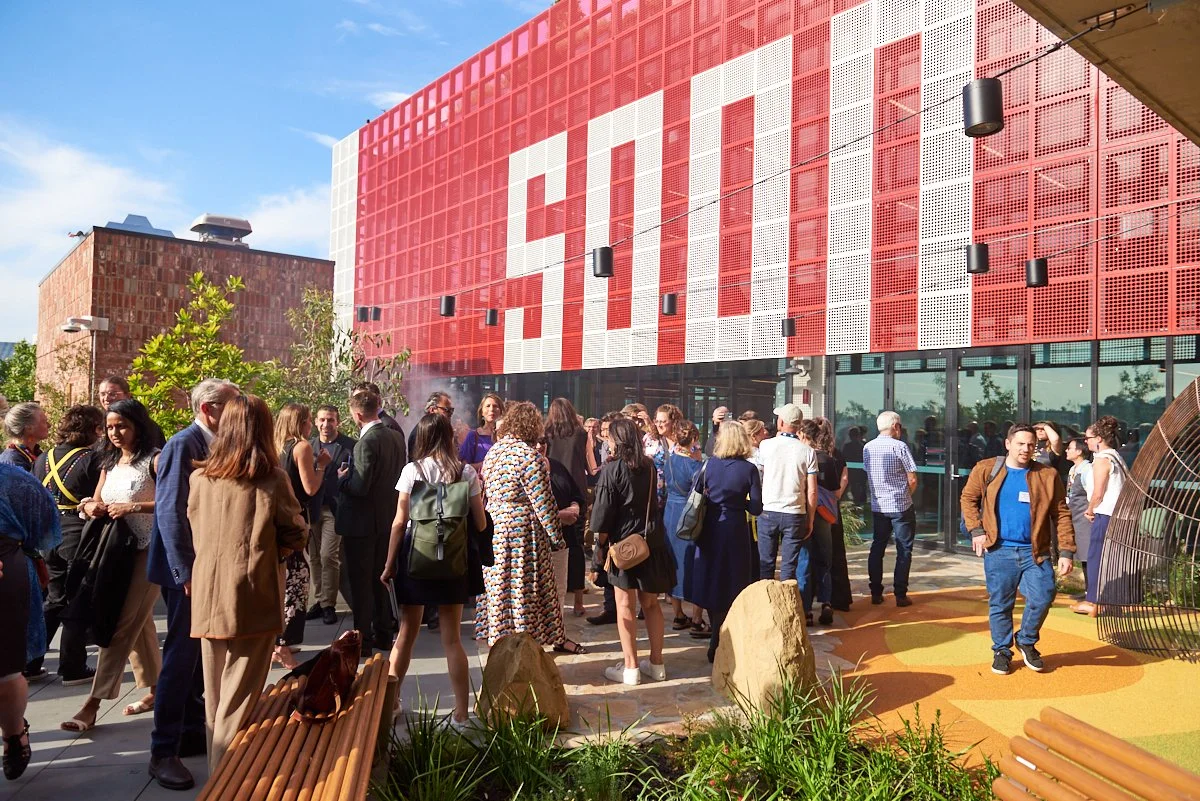People gathered outside a modern building with a large red and white sign that says 'STEM', with some people talking and others walking.