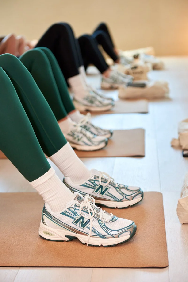 People doing yoga or stretching, wearing athletic shoes and leggings, on mats in a fitness studio.