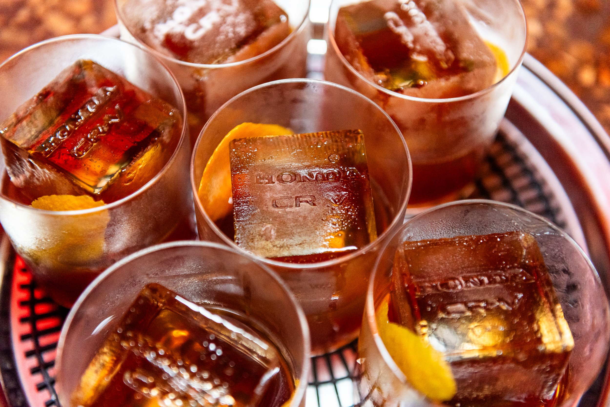 Several glasses of dark-colored beverage with ice cubes and lemon slices on a red tray.