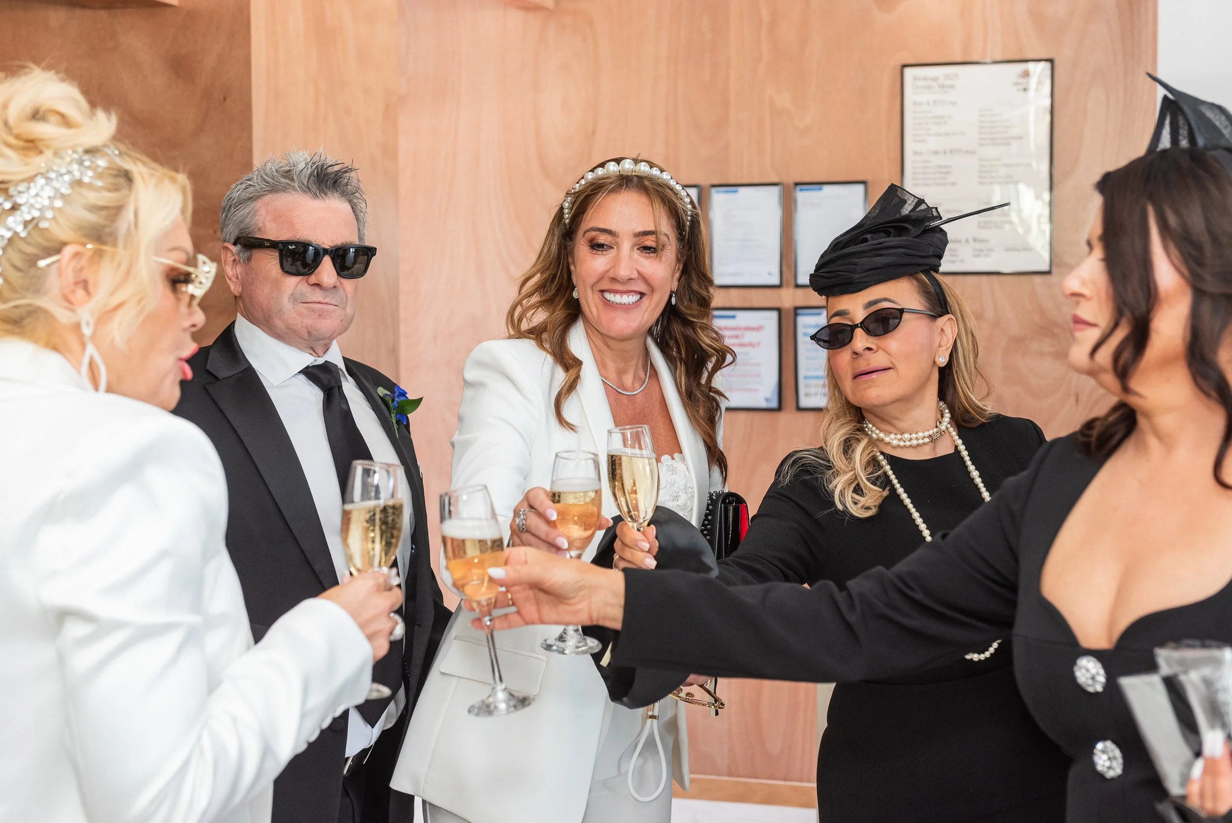 A group of people dressed formally, holding glasses of champagne, celebrating at a social event or wedding reception.