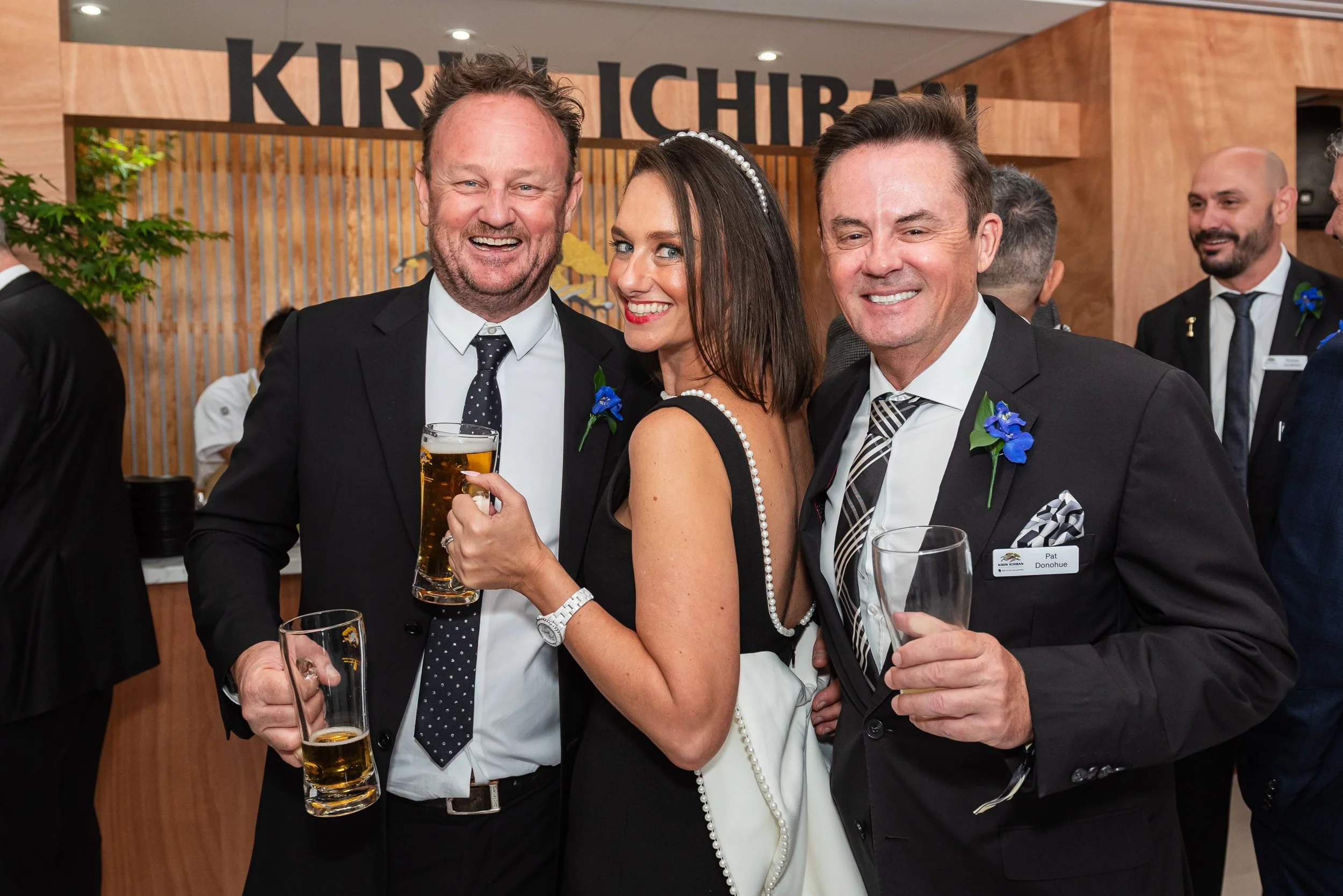 Three people at a formal event, smiling and holding drinks, with a sign that says 'KIRIN CHIBA' in the background.