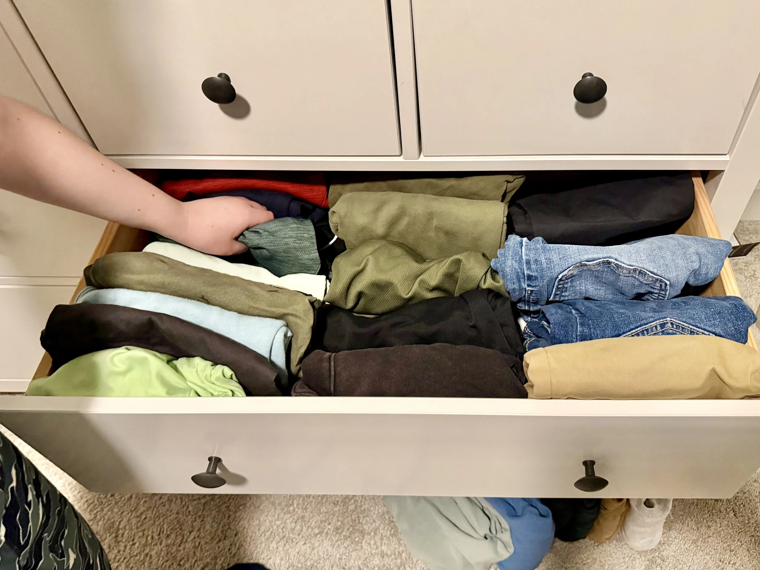 young boy organizing his clothing in a drawer using marie kondo's file folding technique