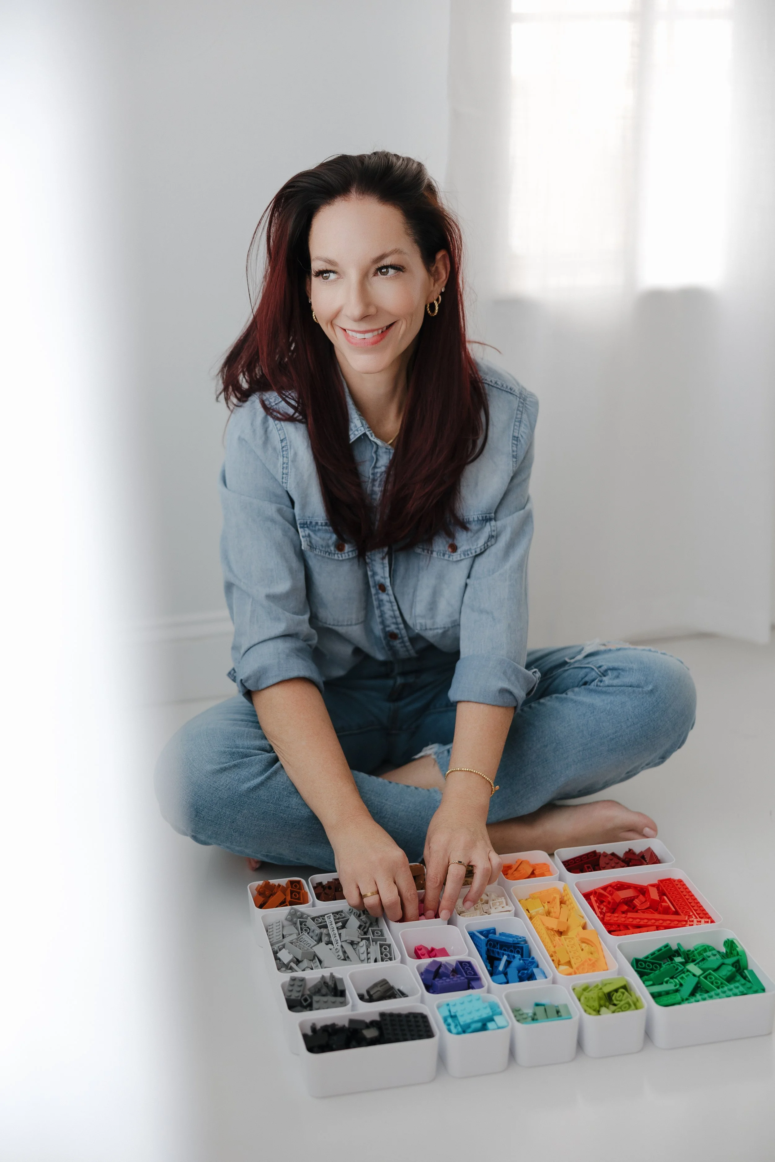 konmari marie kondo tidying consultant in jeans sorting LEGO into a rainbow organization and smiling