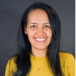 Smiling woman with long black hair wearing a yellow top, against a dark gray background.