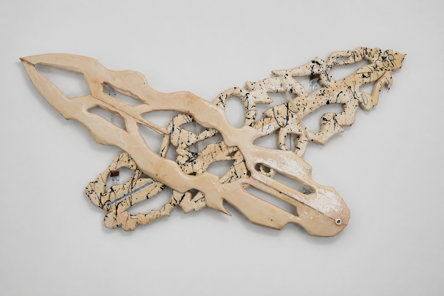 2 surfboard sculptures resembling a in a x formation with a beige base color and black splatter details, mounted on a plain white wall.