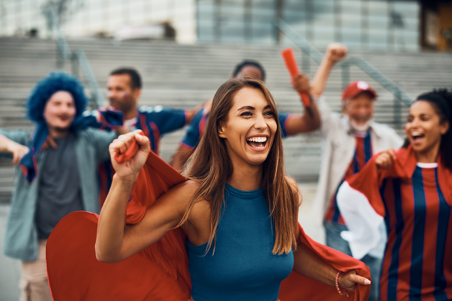 Group of happy sports fans celebrating on stadium steps, wearing team colors and holding cheering props.