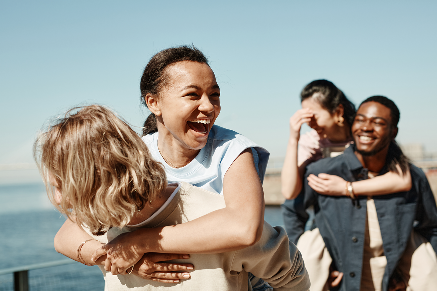 Group of friends outdoors near water, playing and having fun, embracing, smiling, sunny weather