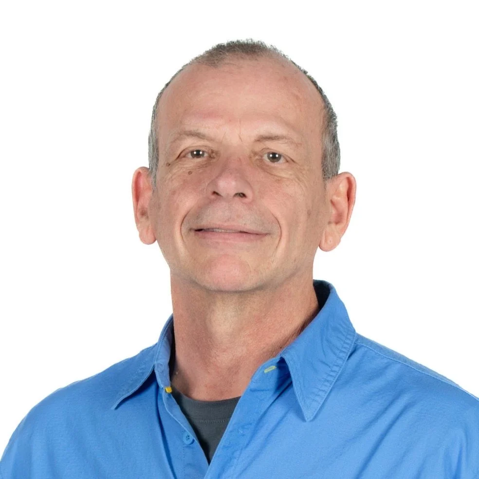 Portrait of a middle-aged man wearing a blue shirt, smiling softly against a white background.