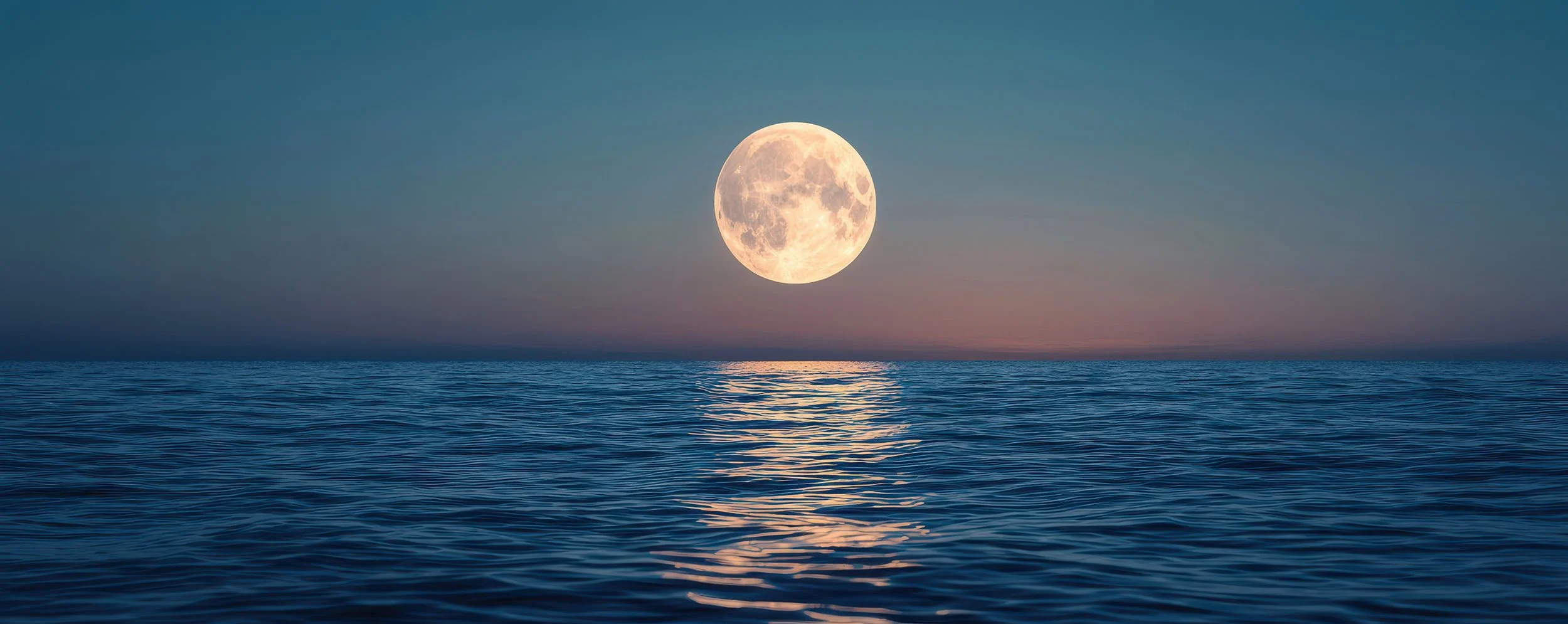 Full moon over the ocean at dusk, with calm water reflecting the moon