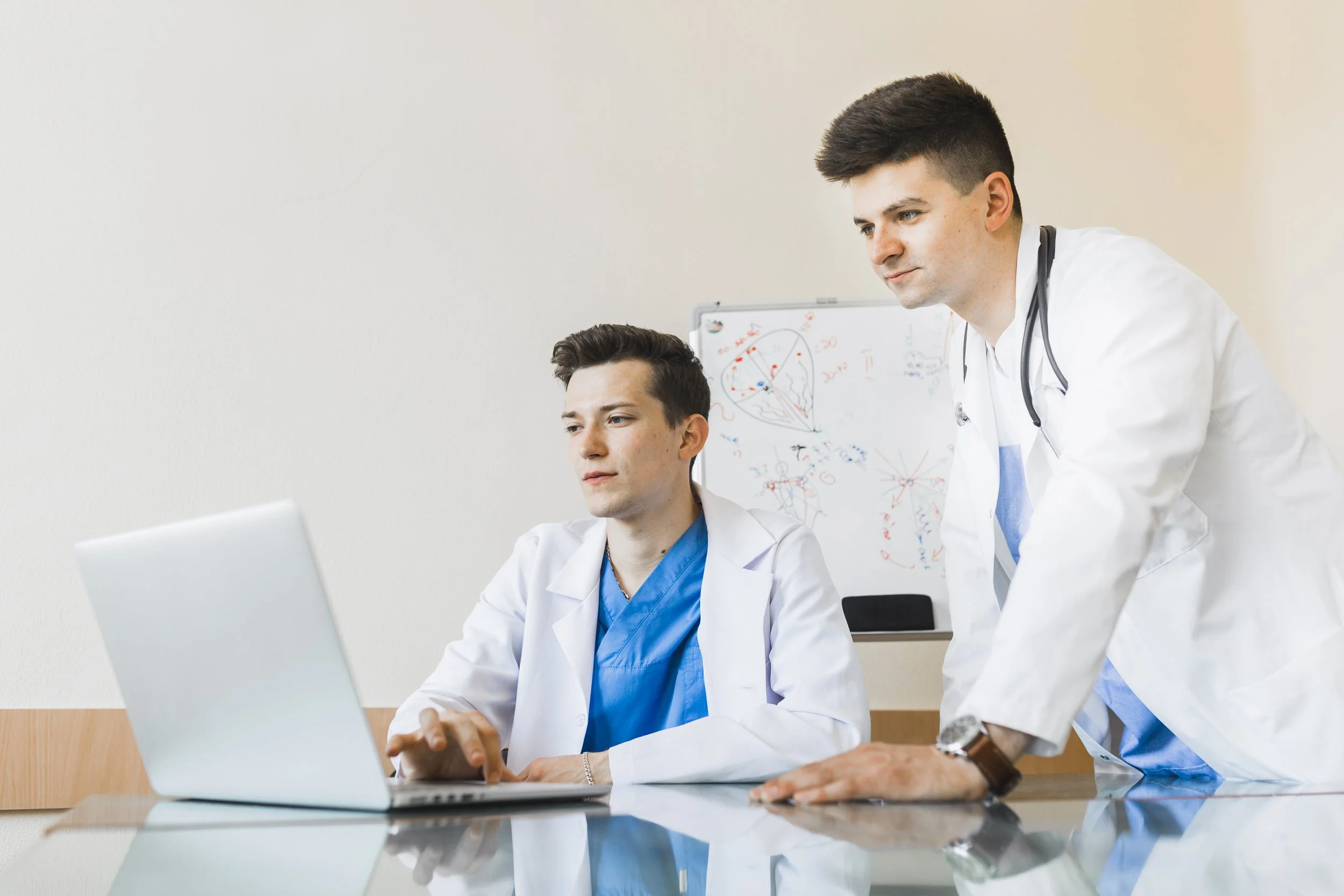 Two male doctors in white coats working together using a laptop in a medical office.