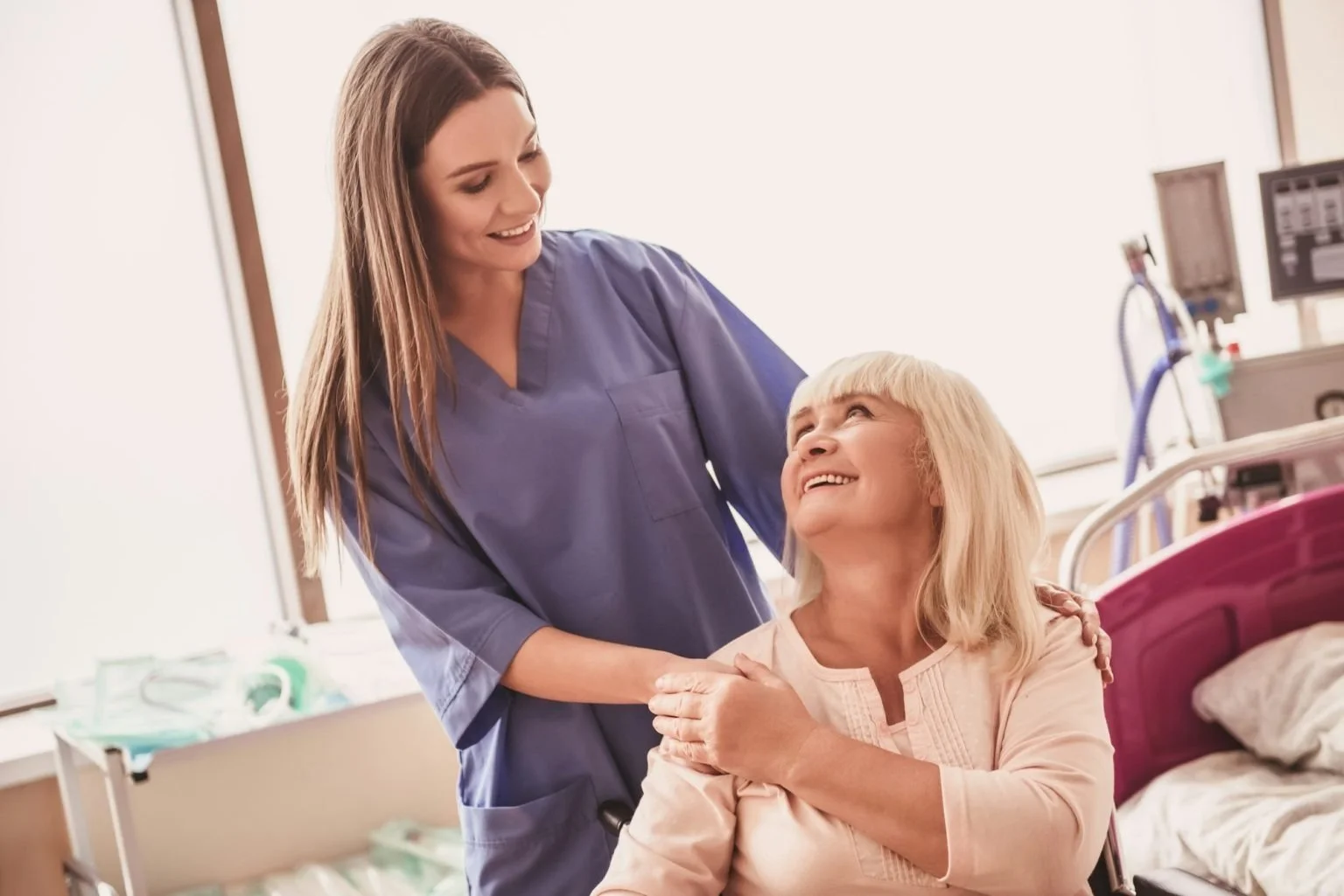 A nurse smiling and talking to an elderly woman in a hospital room.