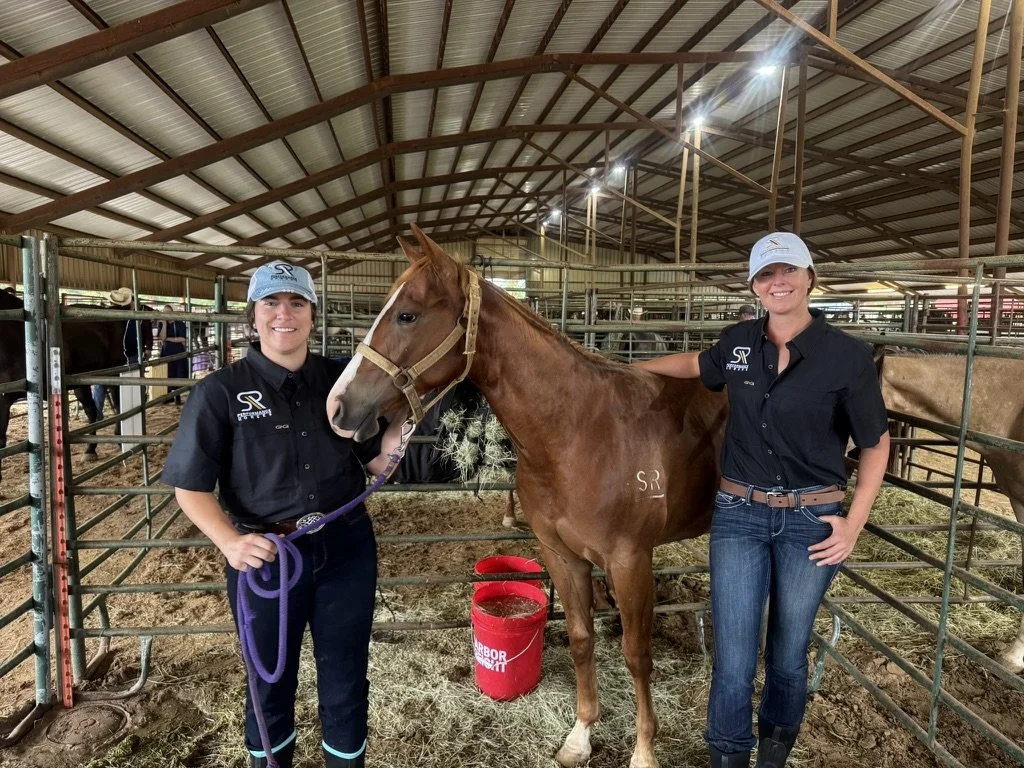 Elizabeth Rose and Michelle standing in a barn with a chestnut horse between them. The woman on the left holds the horse's lead, and the woman on the right has her arm around the horse. SR Bar Ranch Performance Horses Boerne Texas USA