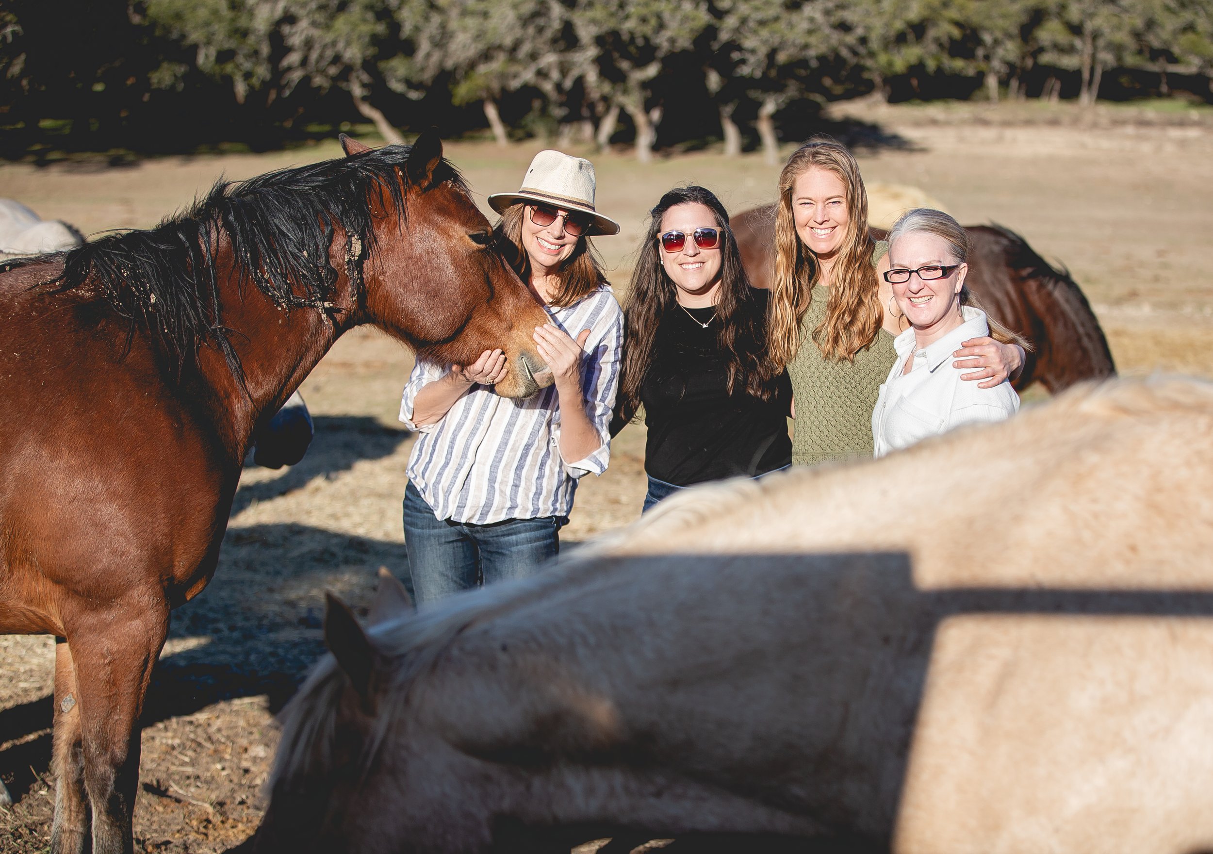 Four women standing outdoors with horses, smiling and posing for the camera. SR Bar Ranch Performance Horses Boerne Texas USA.