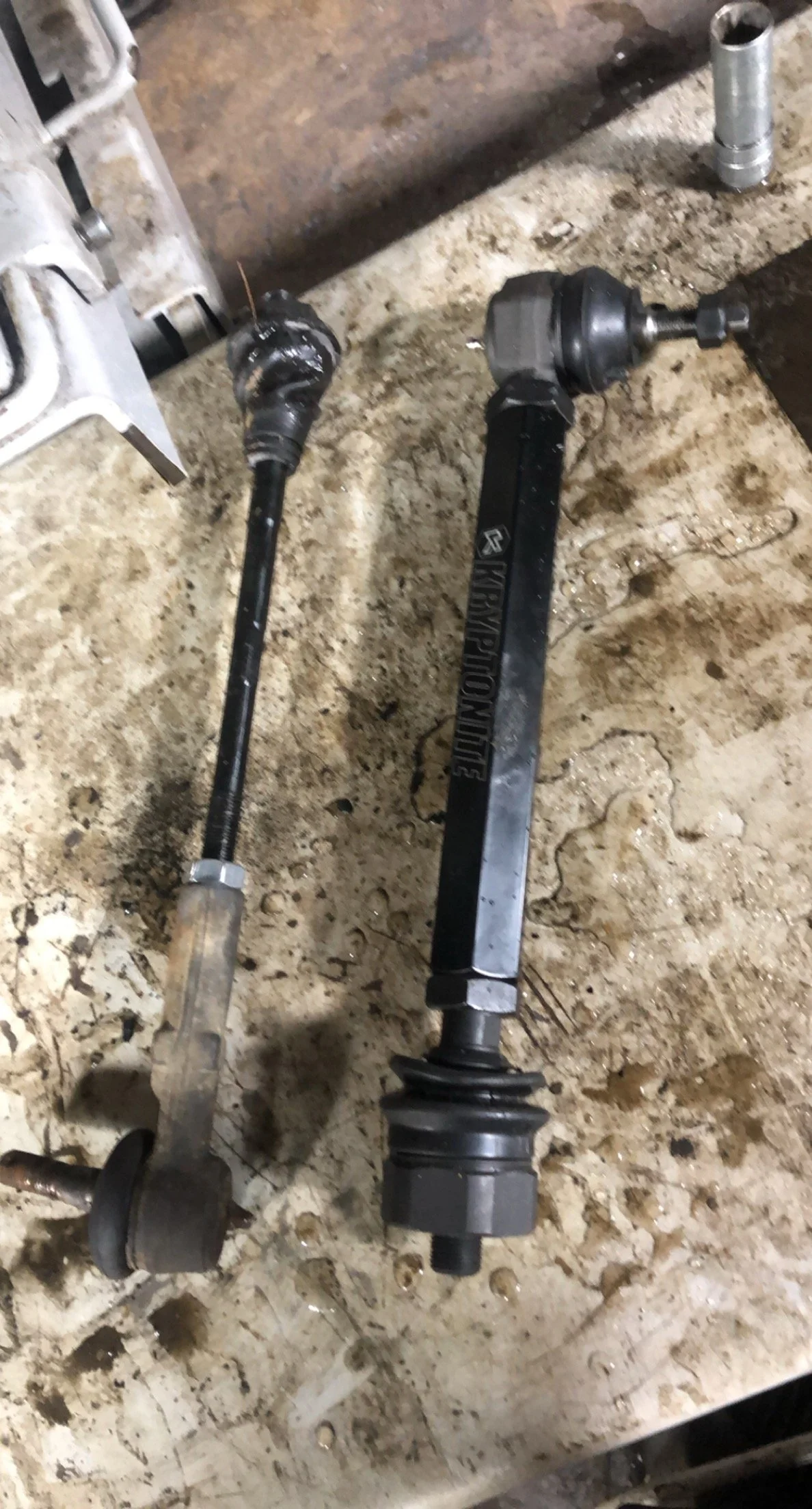 Two automotive driveshafts placed on a dirty workbench in a garage or workshop.