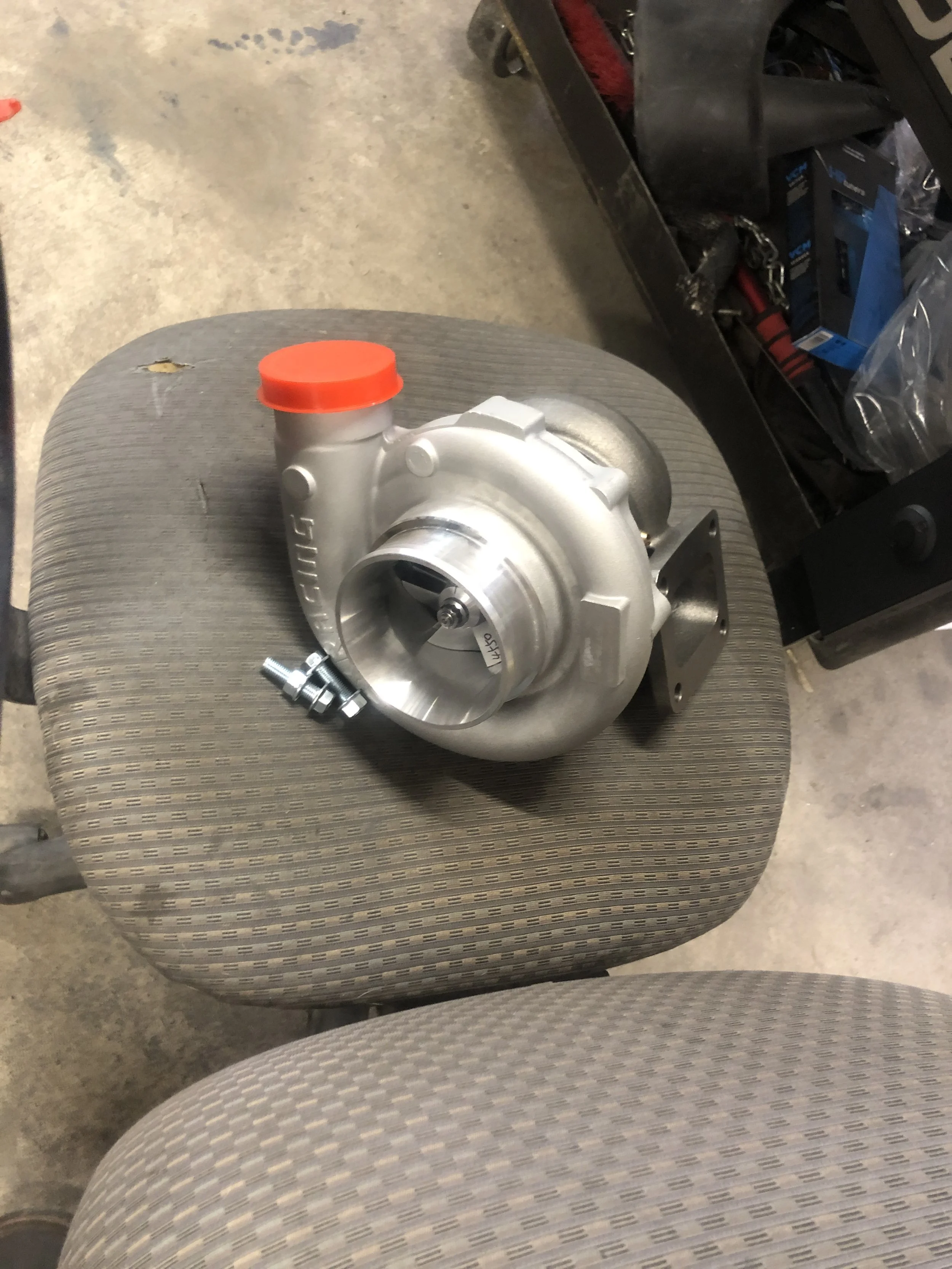 A turbocharger placed on a fabric-covered chair in a workshop setting.