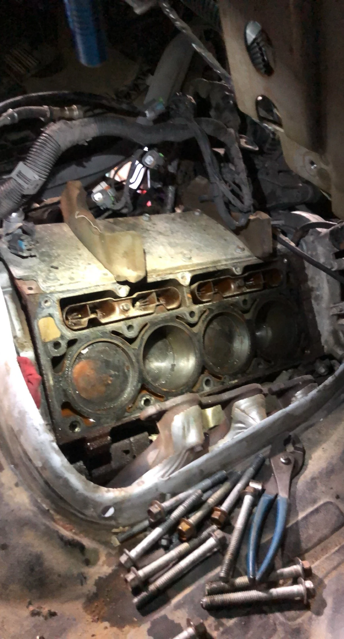 Disassembled engine cylinder head with bolts and used tools nearby.