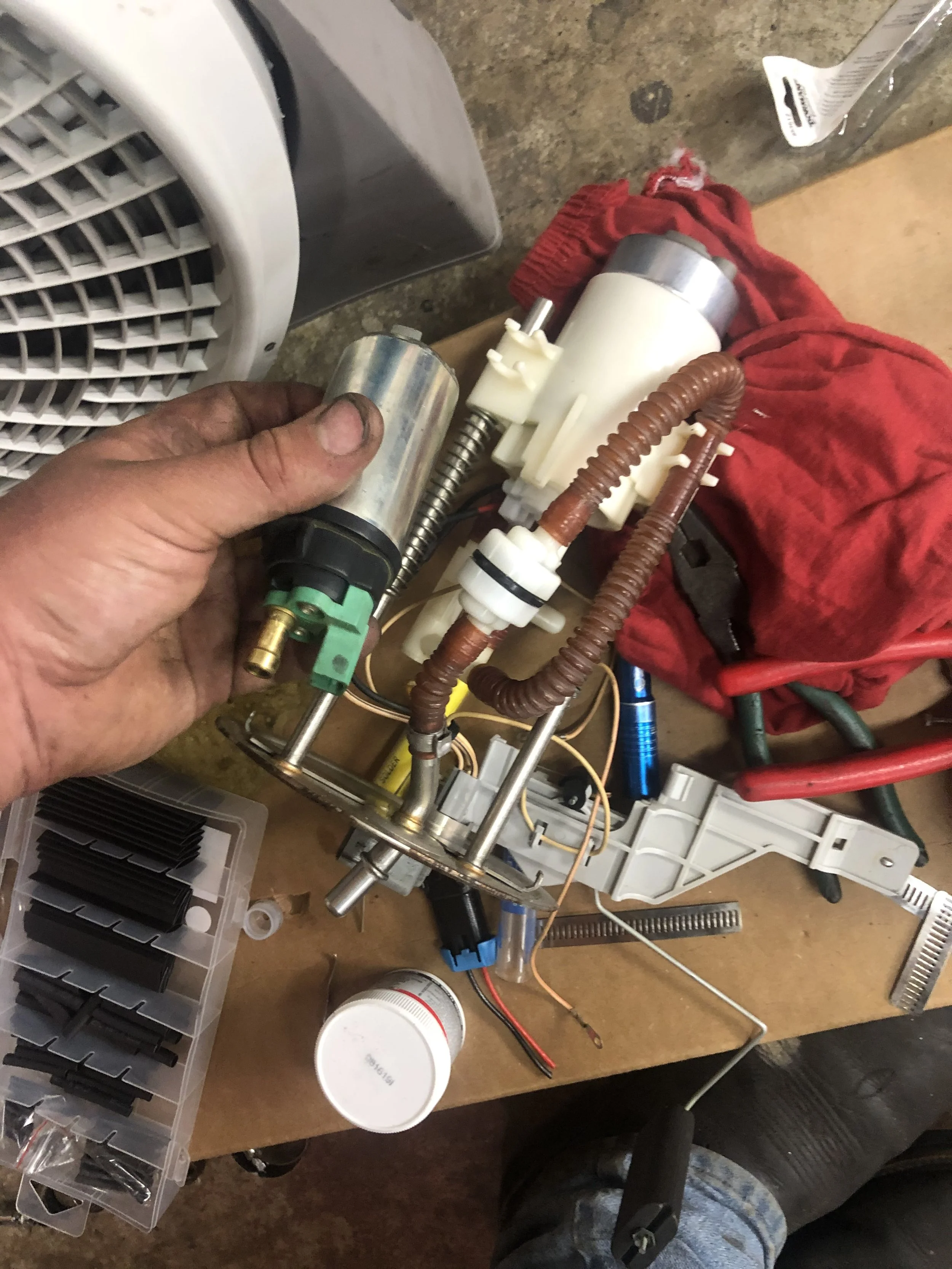 Disassembled fuel pump with various components, wires, and tools on a workbench.