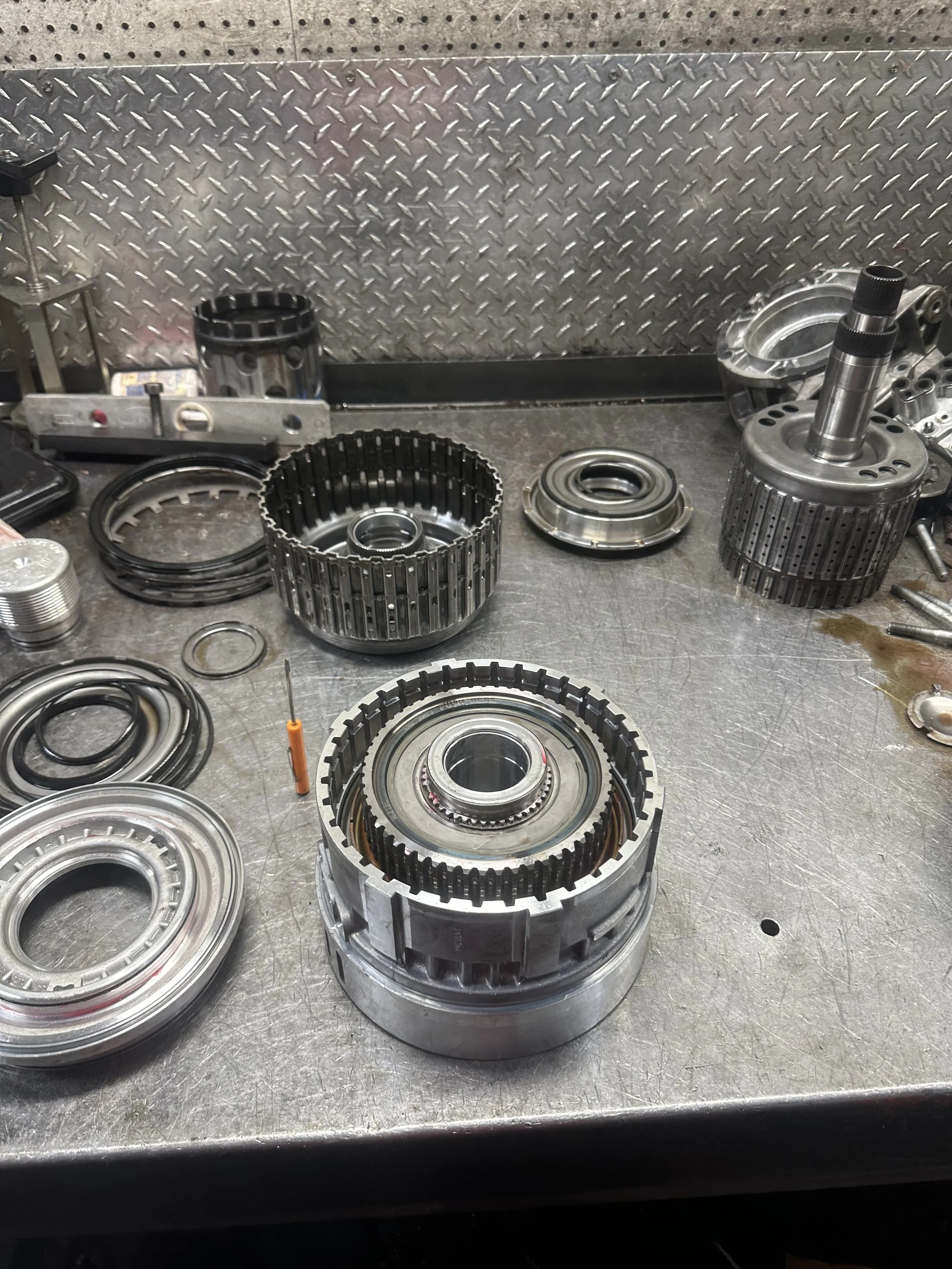 Disassembled automotive transmission parts on a metal workbench, including gears, bearings, seals, and other metal components.
