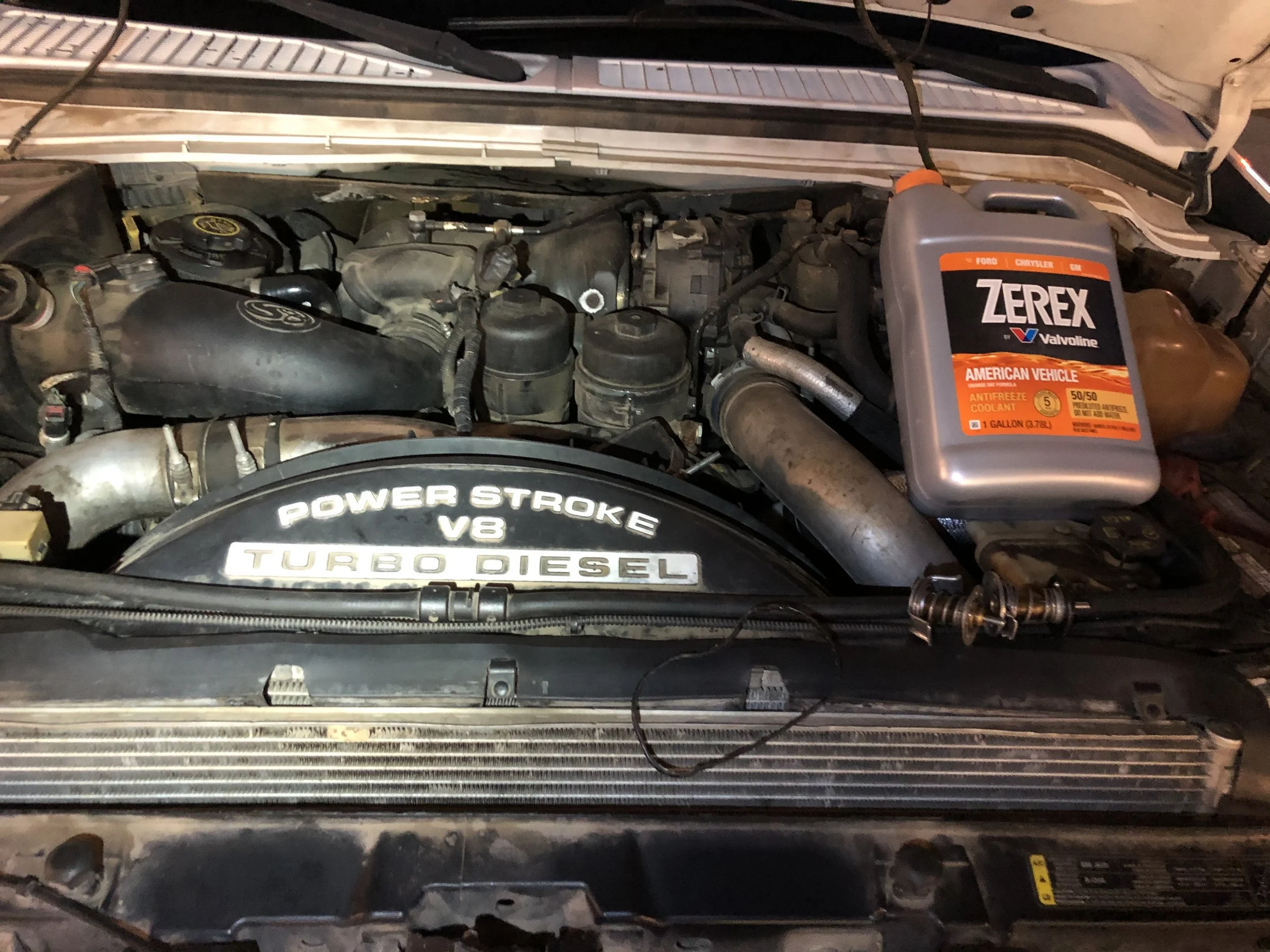 Car engine compartment with a container of Zerex antifreeze coolant placed on top of the engine, which is labeled as a diesel turbo V8 Power Stroke.