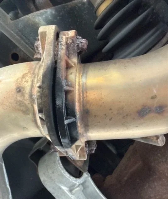 Close-up of a rusty vehicle suspension component and axle with rubber boots and metal parts.