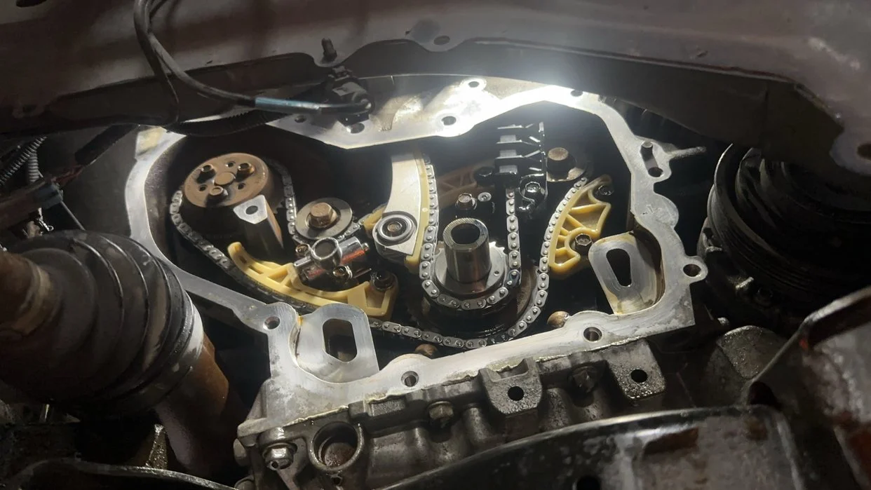 Close-up of an engine's internal components, including timing chain, sprockets, and yellow timing guides, with surrounding engine casing.